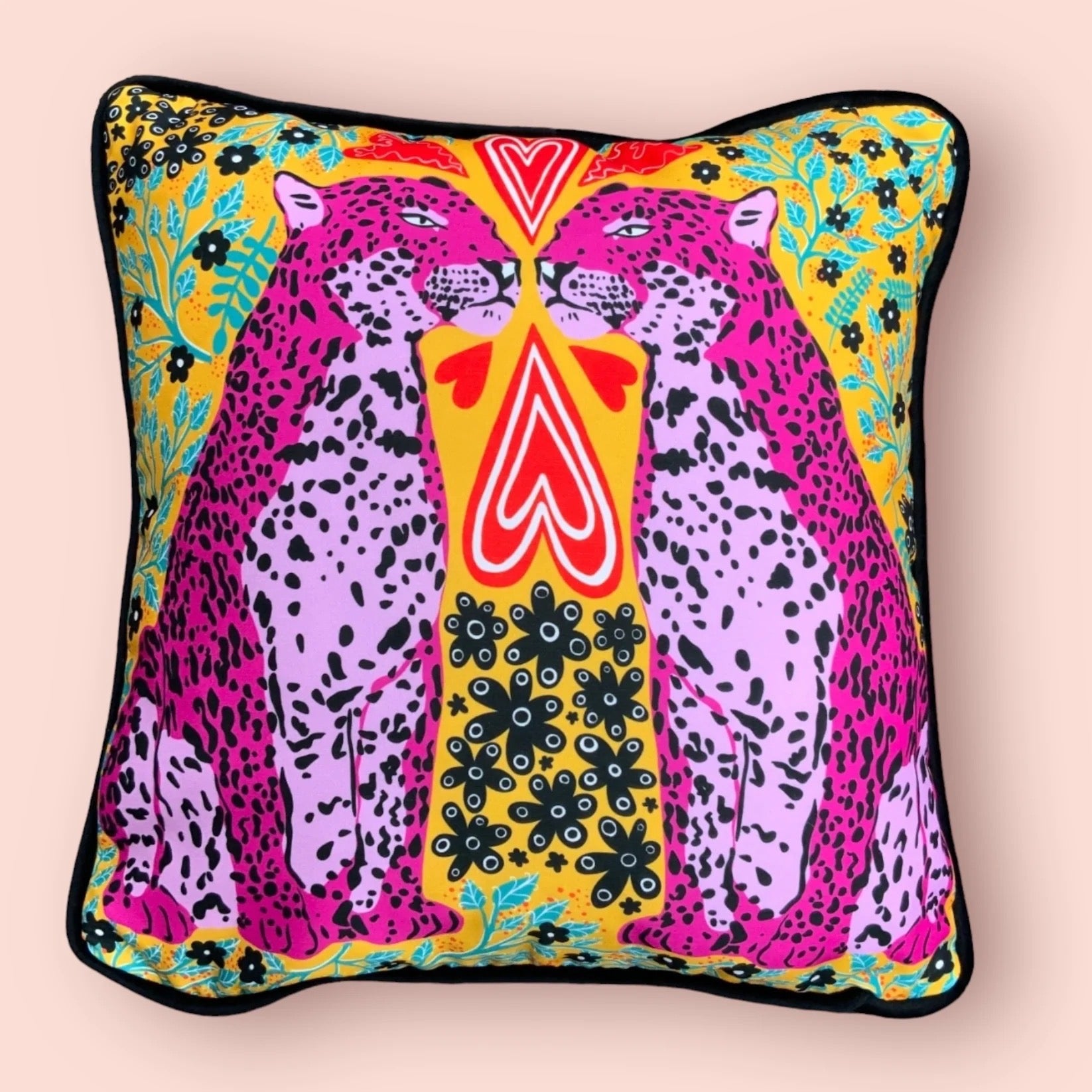Colourful cushion featuring two pink panthers, red love hearts and green and black flowers against a mustard background, on a light pink background.