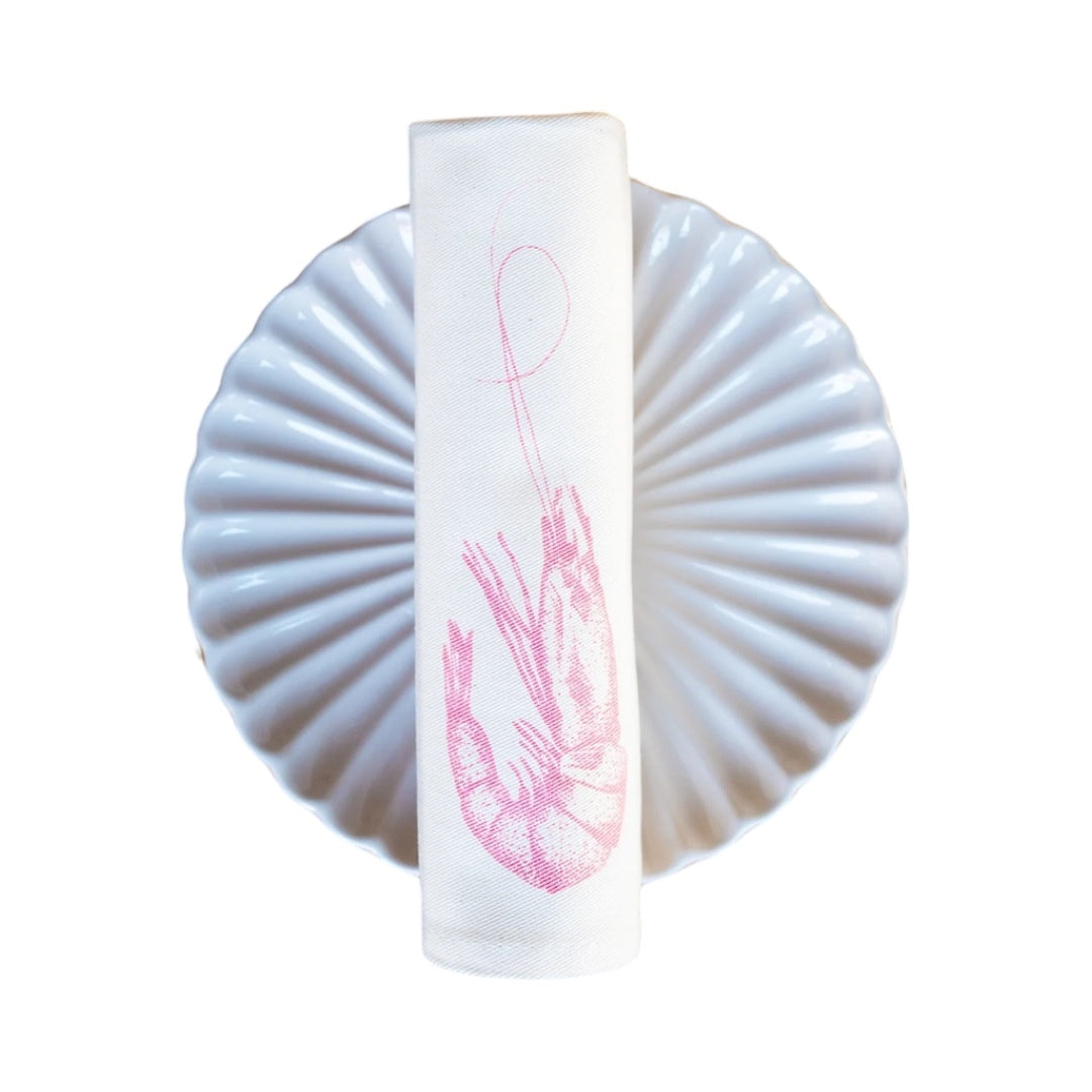 Cream cotton napkin with a pink prawn rolled on a plate.