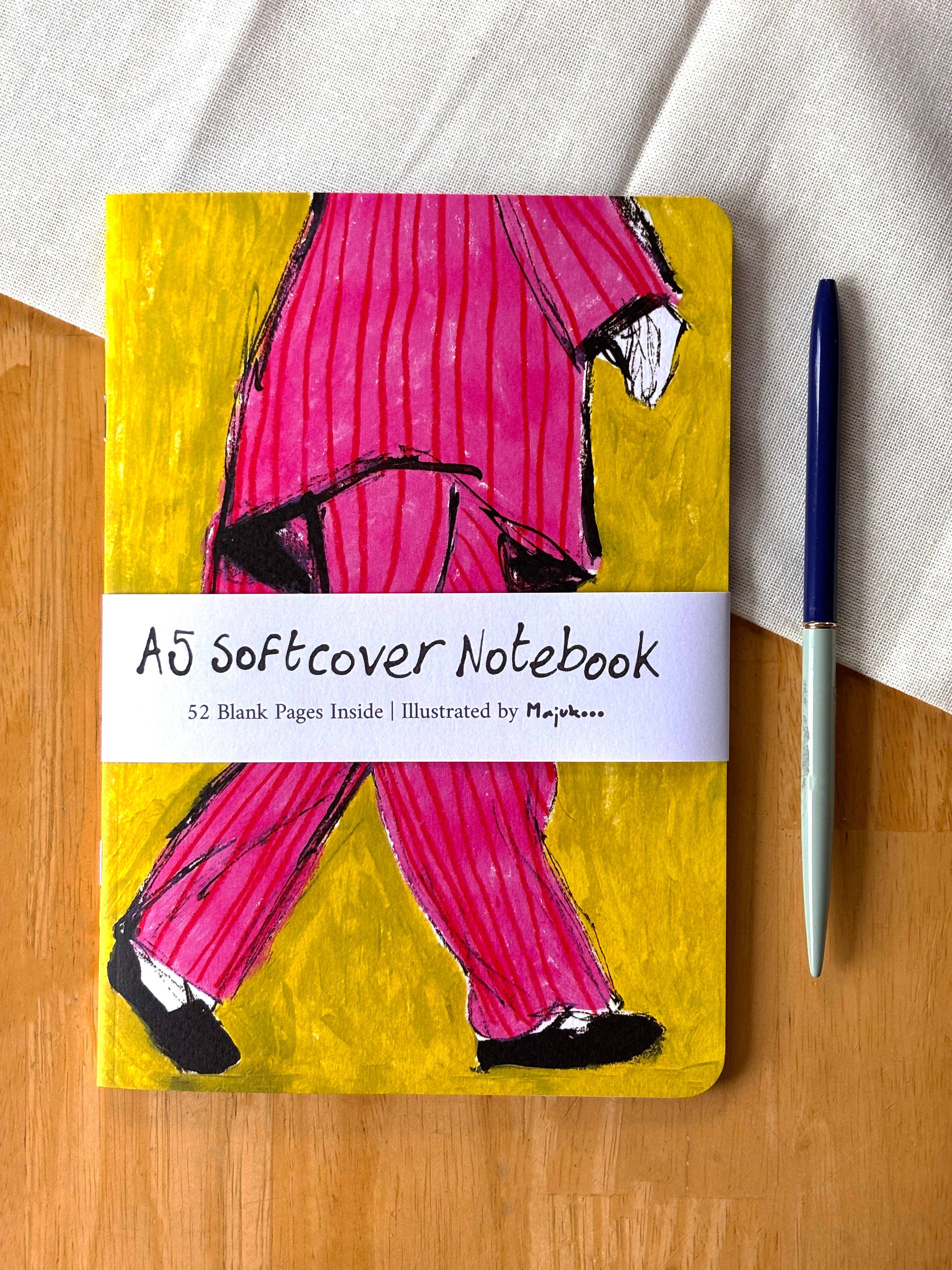 Notebook with a colorful cover featuring a person in pink pants on a wooden surface.