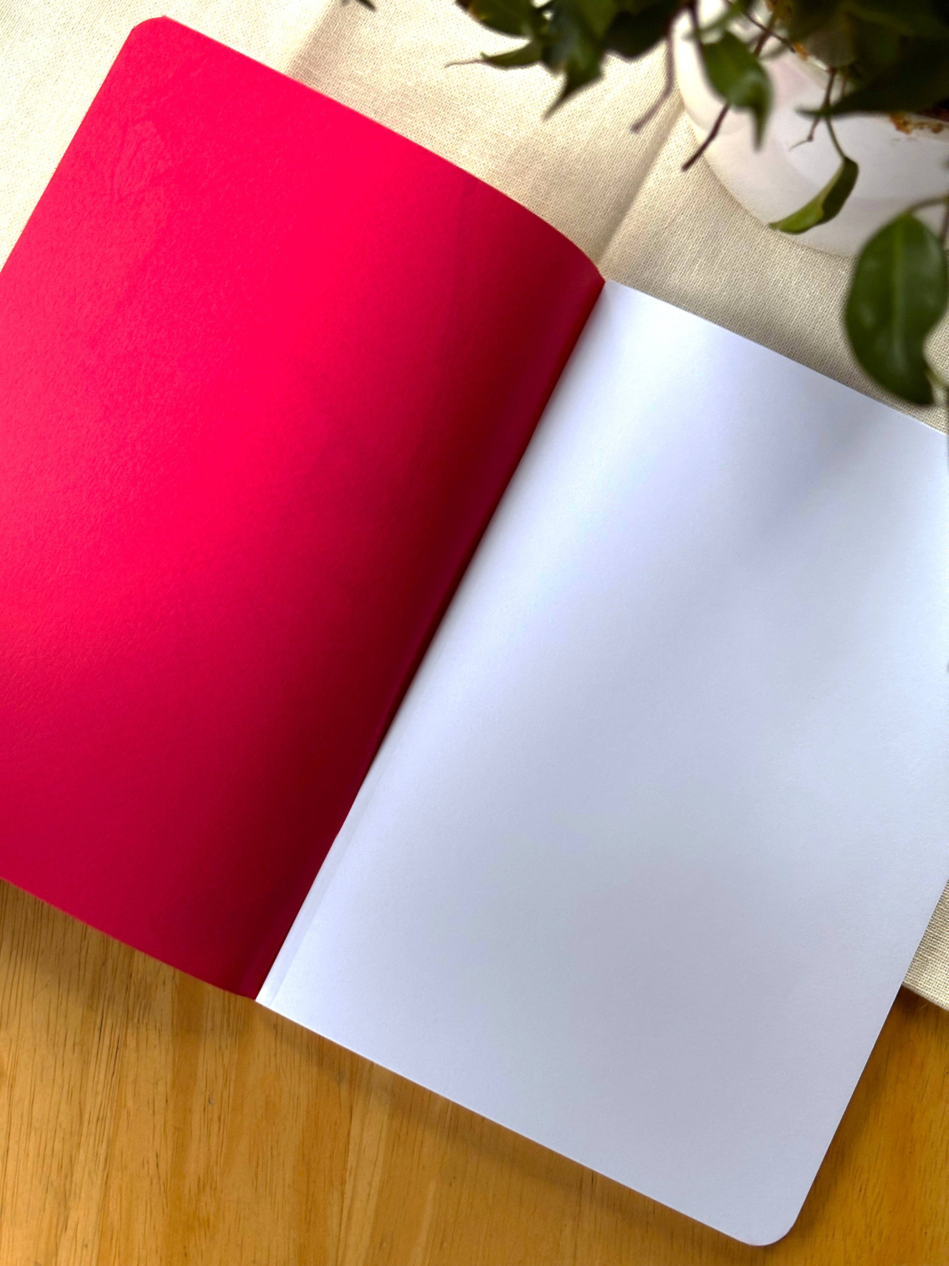 Red and white notebook on a wooden surface with a plant in the background.