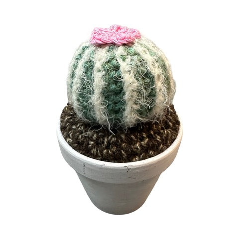Handmade round crochet cactus with a pink flower in a white painted terracotta pot.