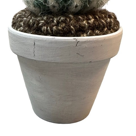 Handmade round crochet cactus with a pink flower in a white painted terracotta pot.
