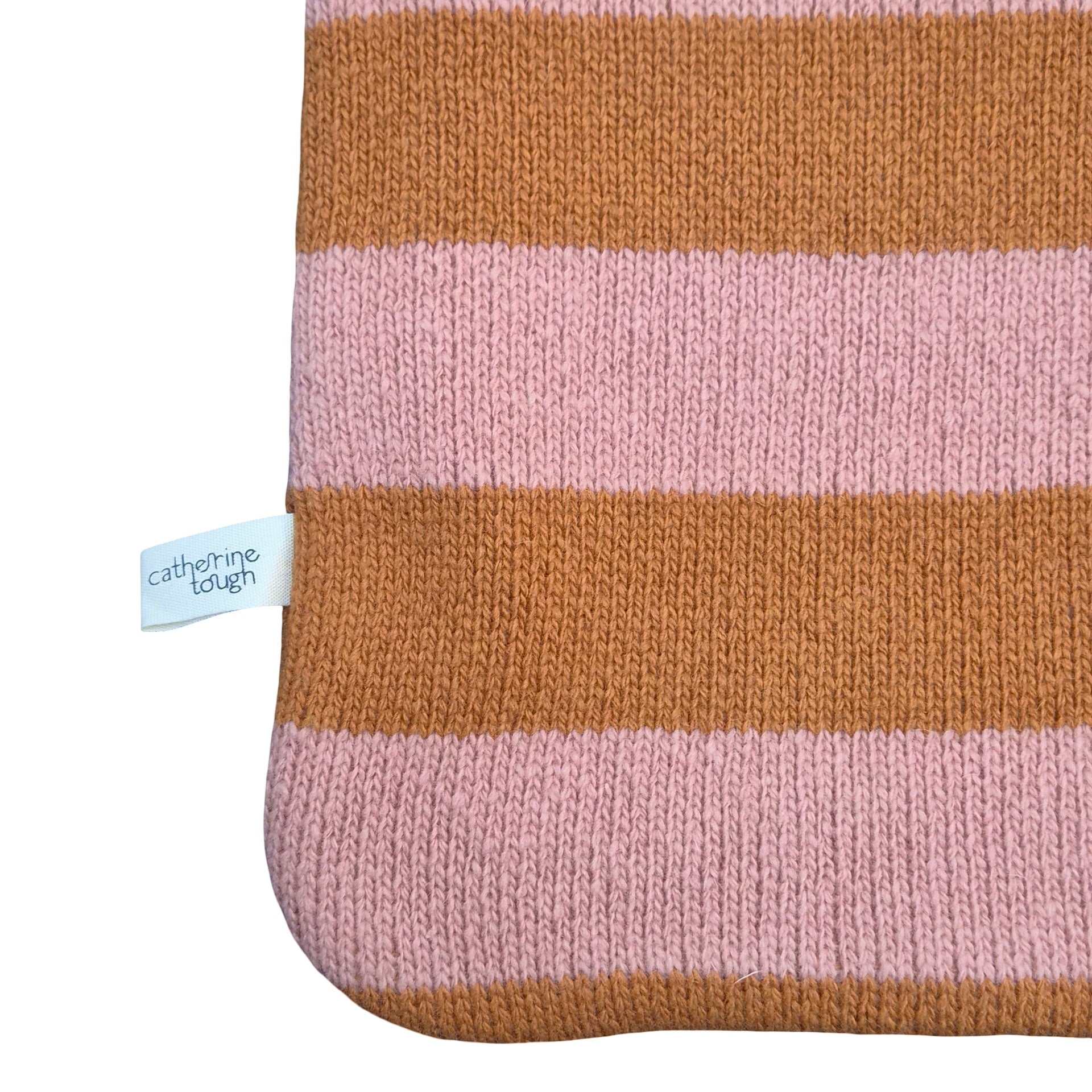 A close-up of a knitted textile with alternating horizontal stripes in warm orange and soft dusty pink, shown on a white background with a small sewn label reading 'catherine tough'.