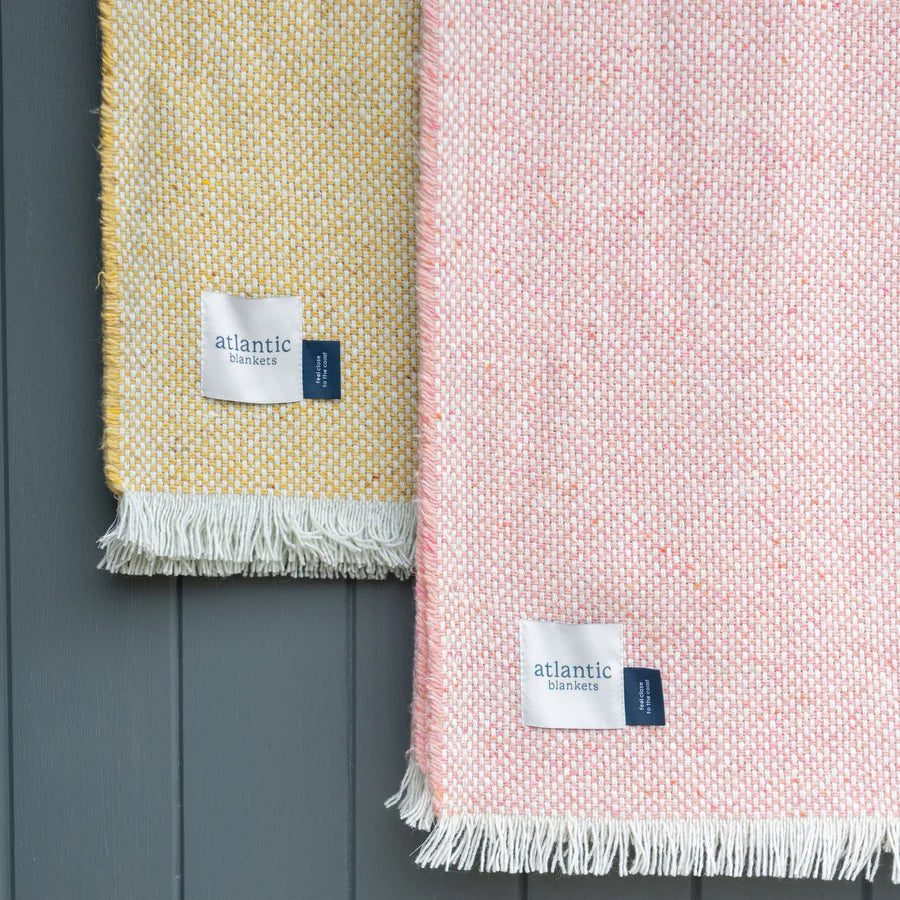 Pink and yellow blankets with white fringe on a grey background, featuring Atlantic Blankets labels.