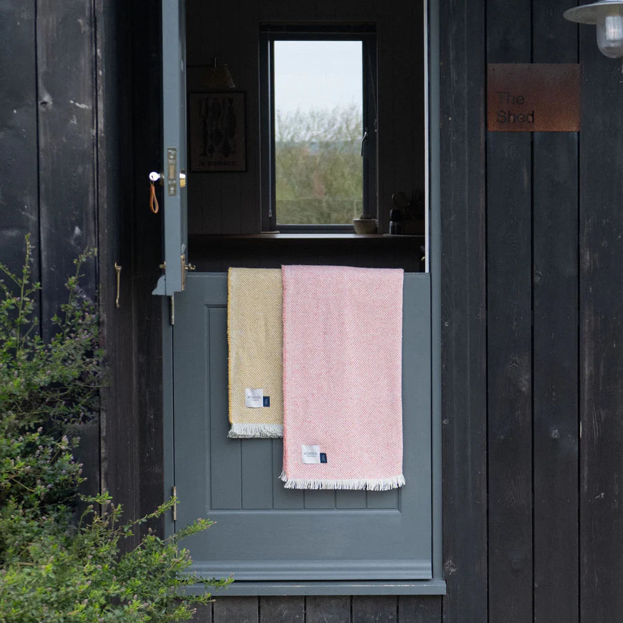 Pink and yellow blankets hanging on a wooden door with a view of greenery outside.