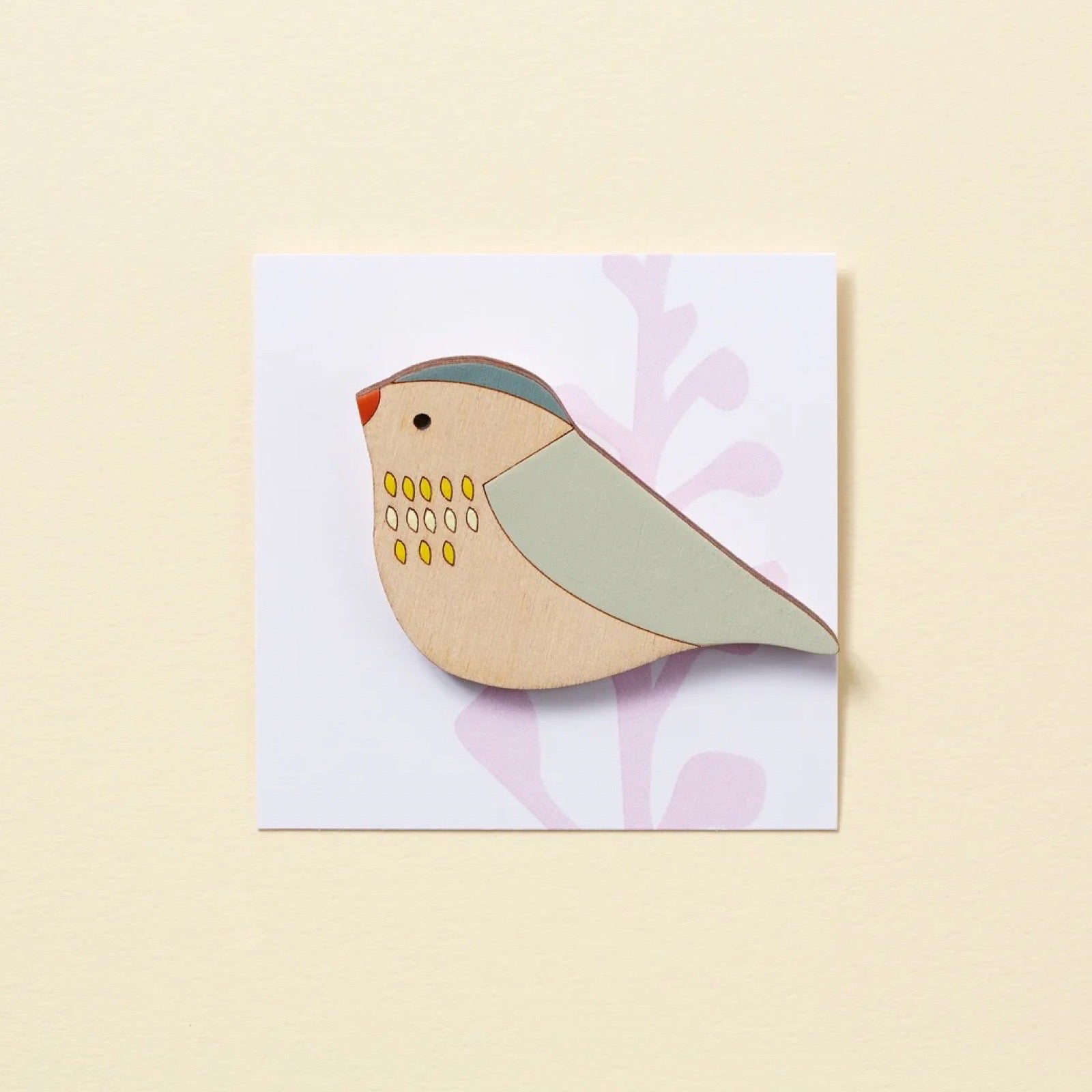 Wooden bird brooch on a card with a floral design on a beige background.