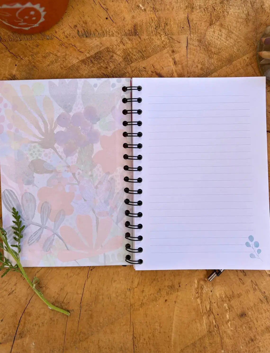 A spiral-bound lined notebook with a floral pattern on the cover, placed on a rustic wooden surface.