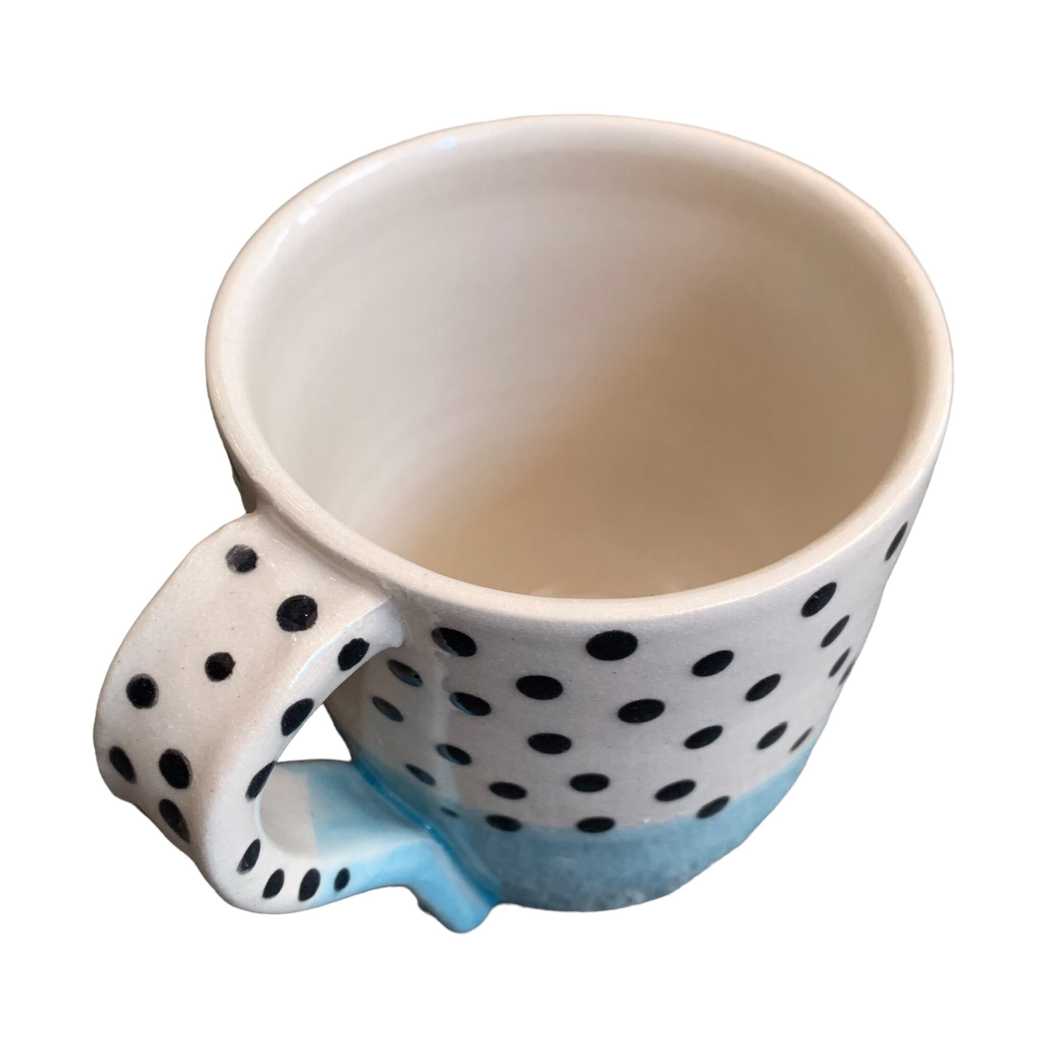 The top of a handmade mug with a pale blue glaze up to the centre and black polka dots on a white background on the top half.