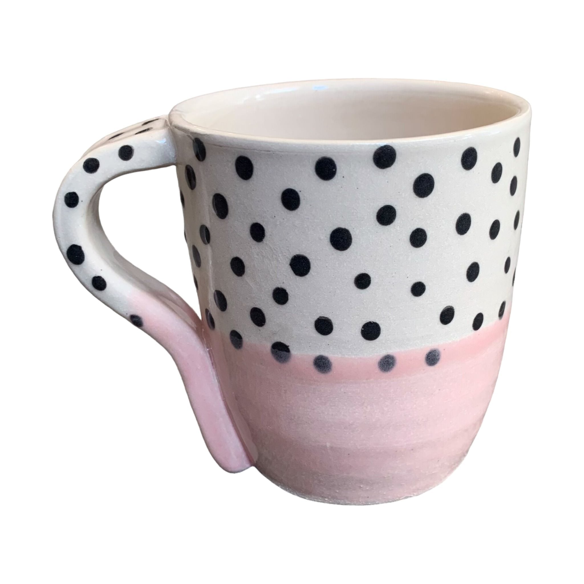 A handmade mug with a pale pink glaze up to the centre and black polka dots on a white background on the top half.