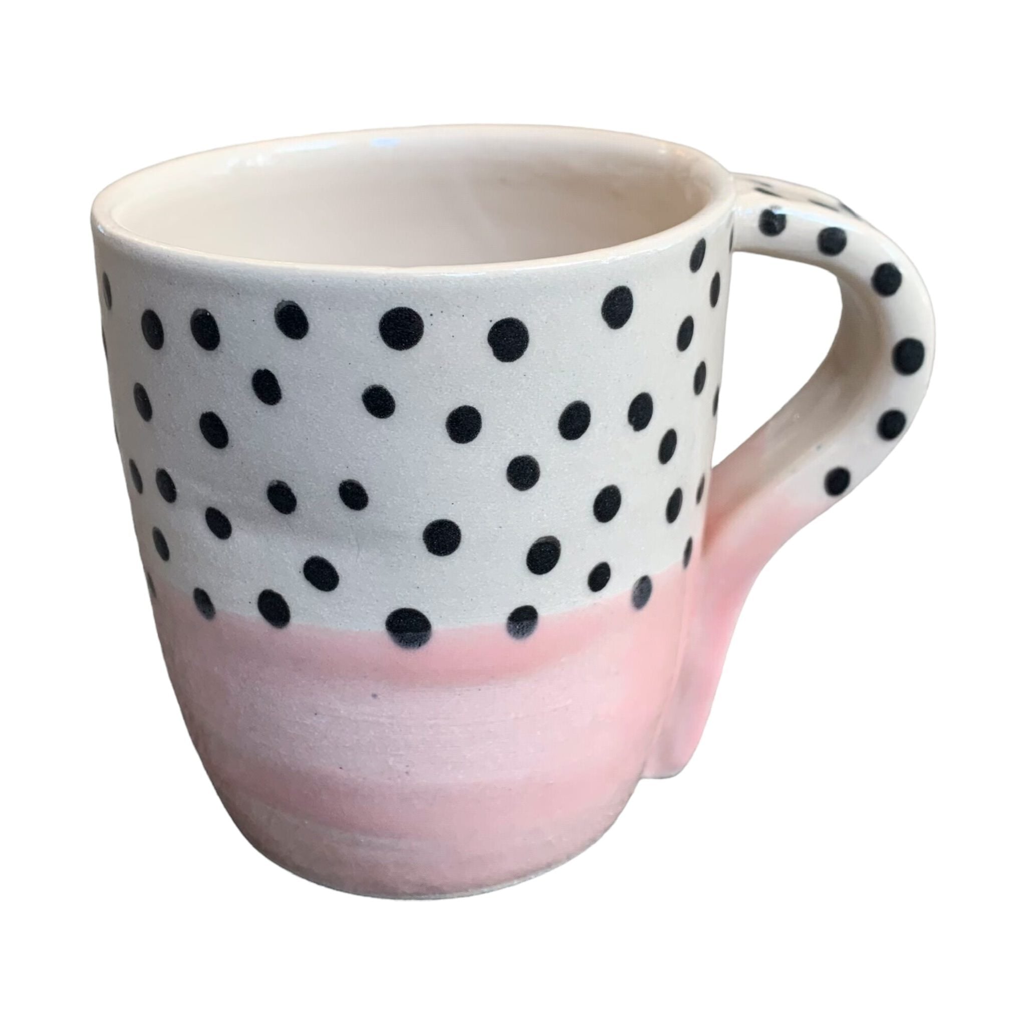 A handmade mug with a pale pink glaze up to the centre and black polka dots on a white background on the top half.