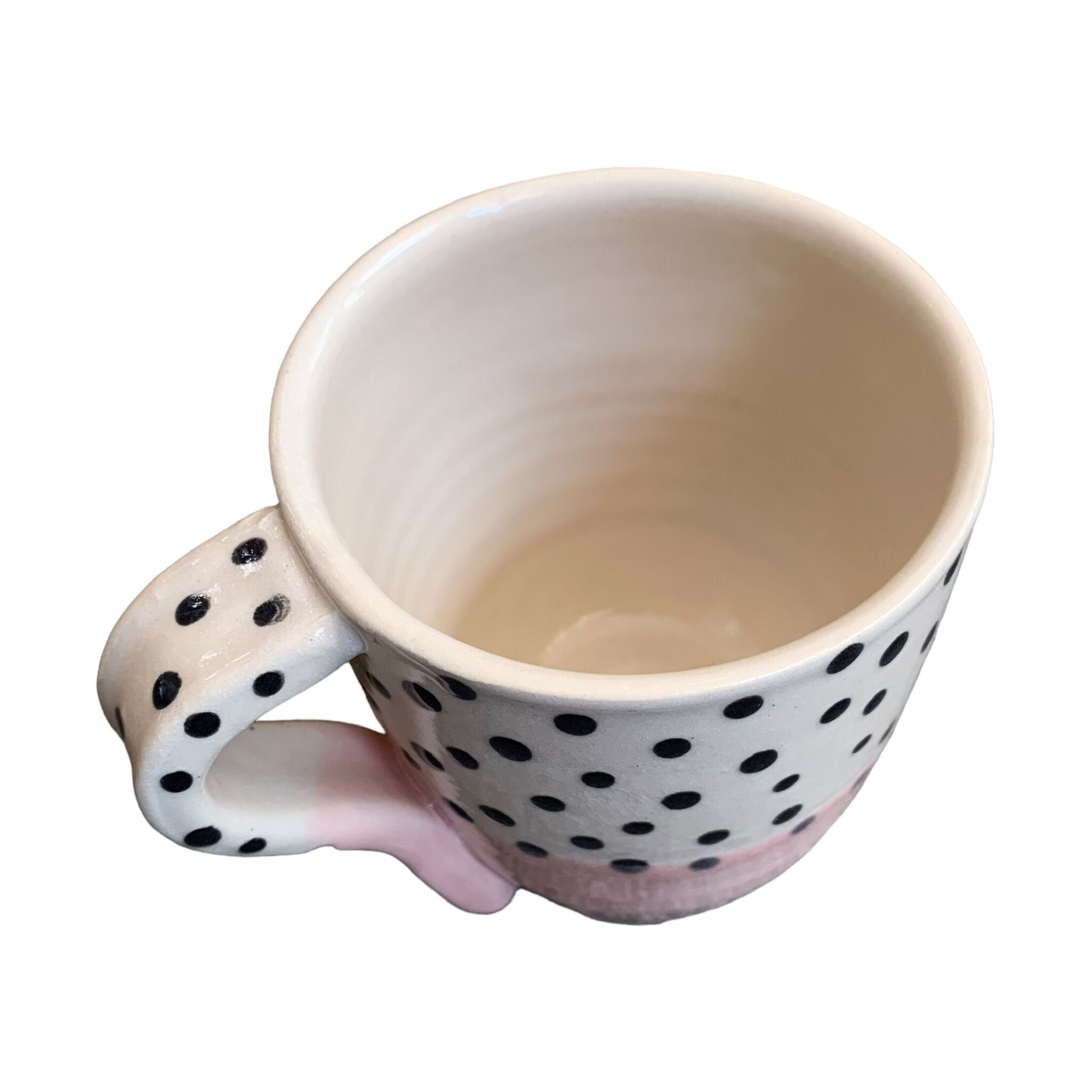 The top of a handmade mug with a pale pink glaze up to the centre and black polka dots on a white background on the top half.
