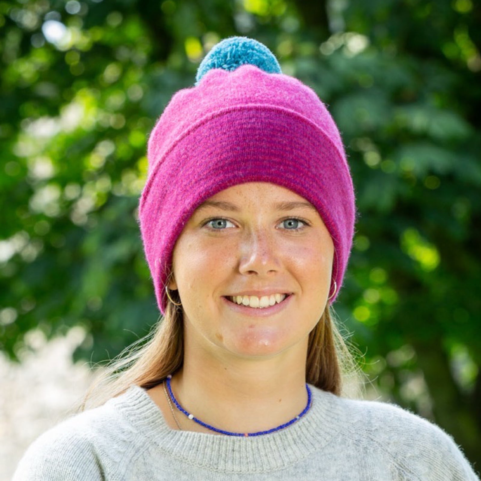 Person wearing a pink beanie with a blue pom-pom outdoors.