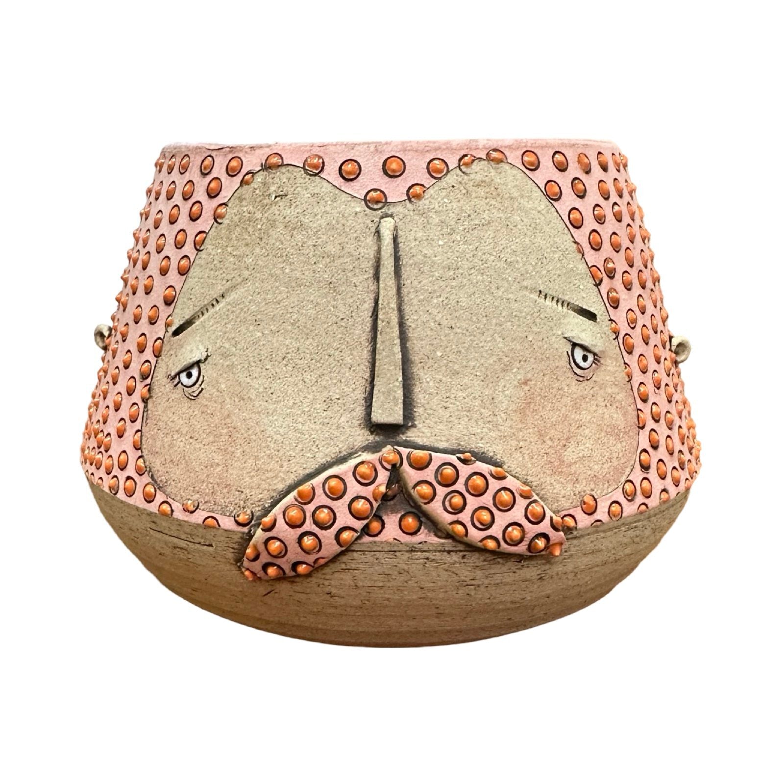 A handmade ceramic mug with a carved man's face and moustache, glazed in pink with a red diamond design.