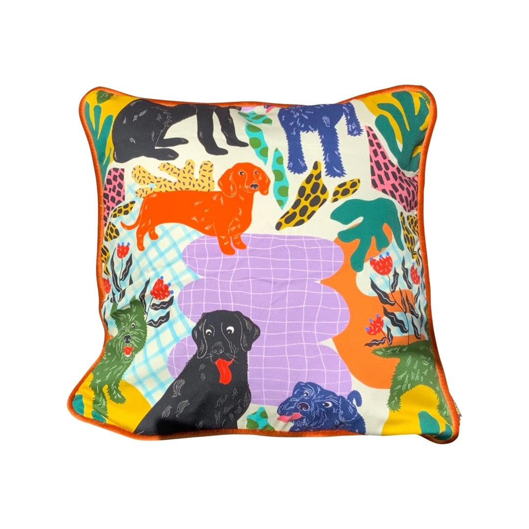 Colourful cushion featuring black labradors, orange dachshunds and green scottie dogs with green leaves and a lilac background.