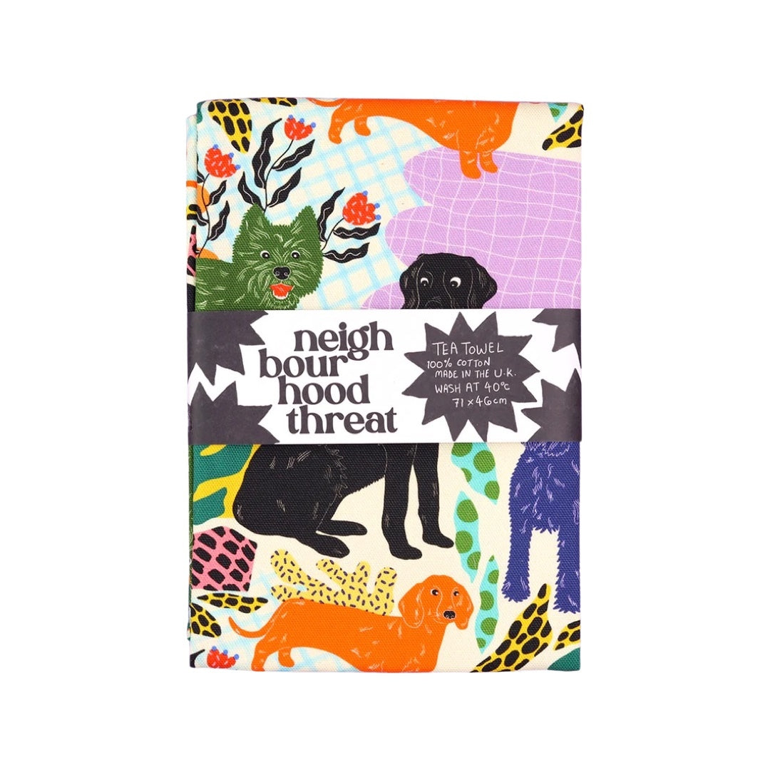 Tea towel featuring black labradors, orange dachshunds and green scottie dogs with green leaves and a lilac background folded with belly band.