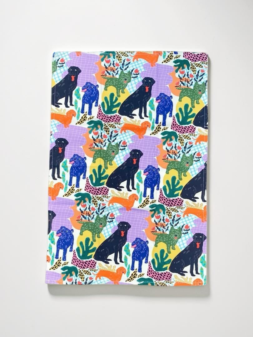 Colourful tea towel with dog and plant pattern on a white background.