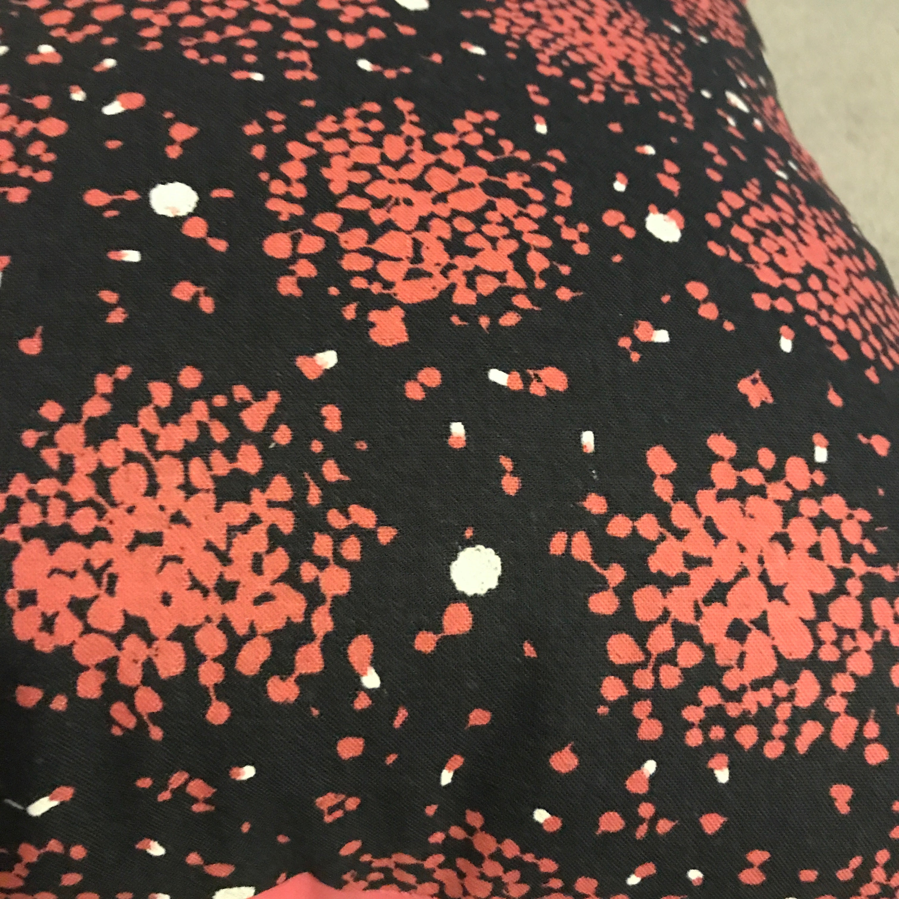 A cushion cover with a charcoal background featuring irregular pops of pink pattern.