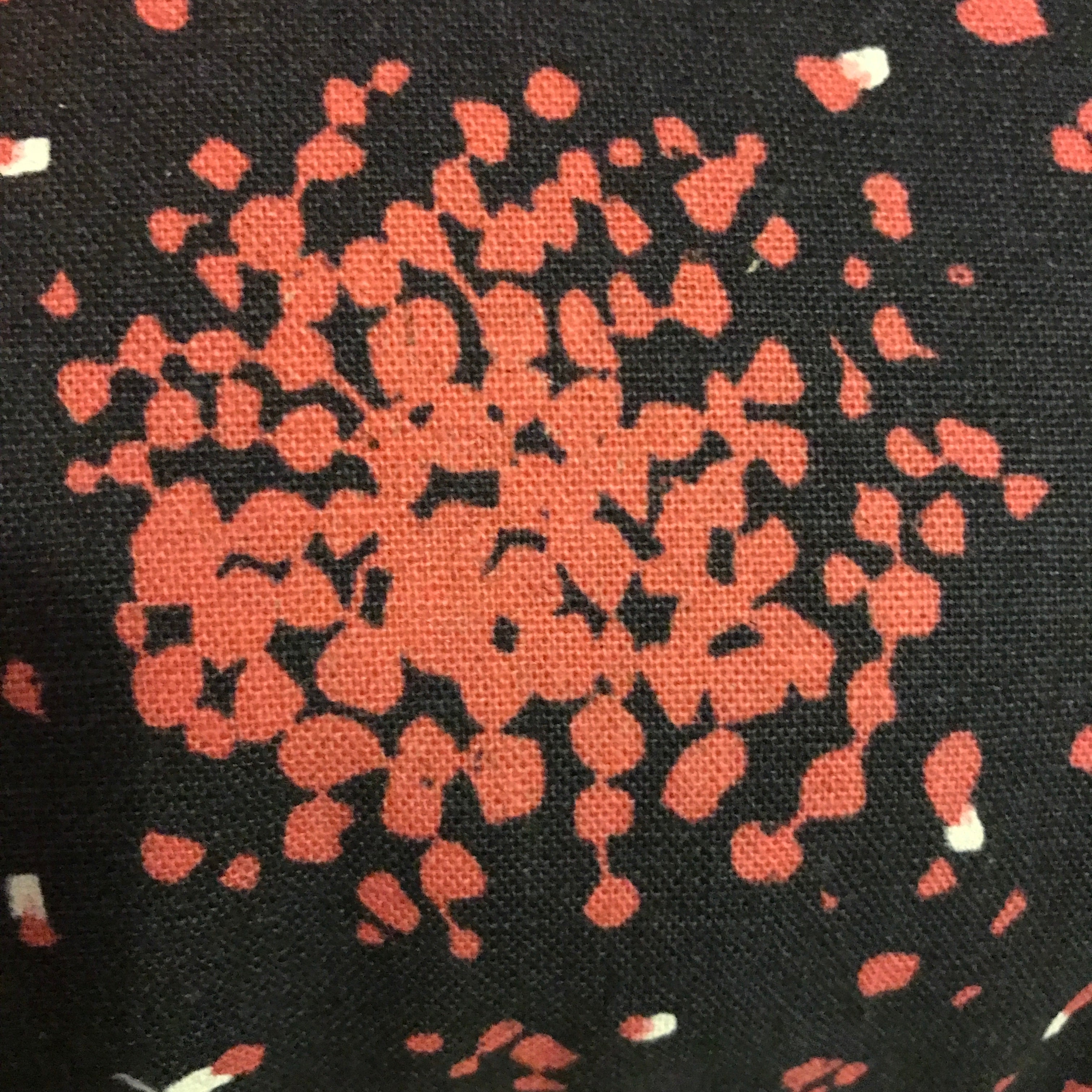 A cushion cover with a charcoal background featuring irregular pops of pink pattern.