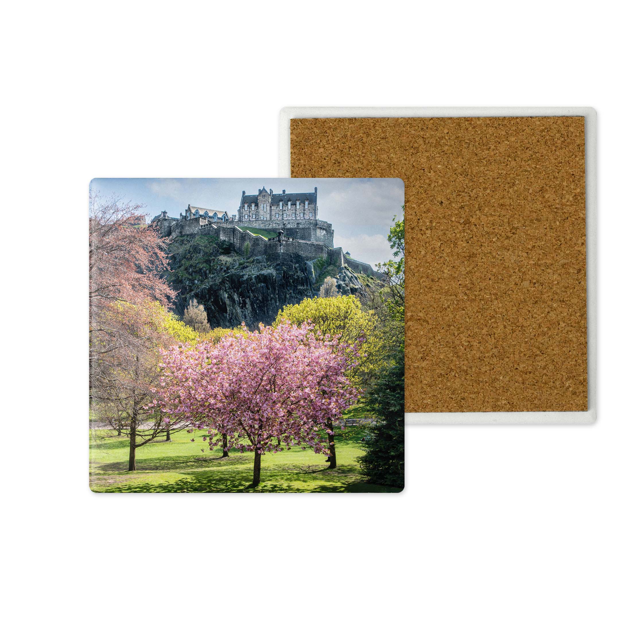 A square coaster featuring a printed landscape photo of Edinburgh Castle on a rocky hill with pink flowering trees in the foreground, shown next to the back of another coaster with a brown cork surface on a white background.