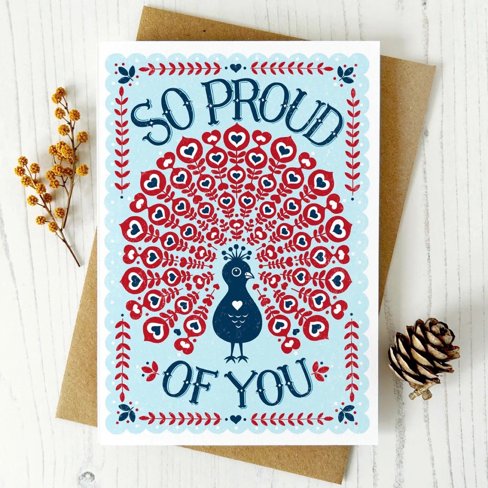Greeting card with a peacock design and 'So Proud of You' text on a white background.