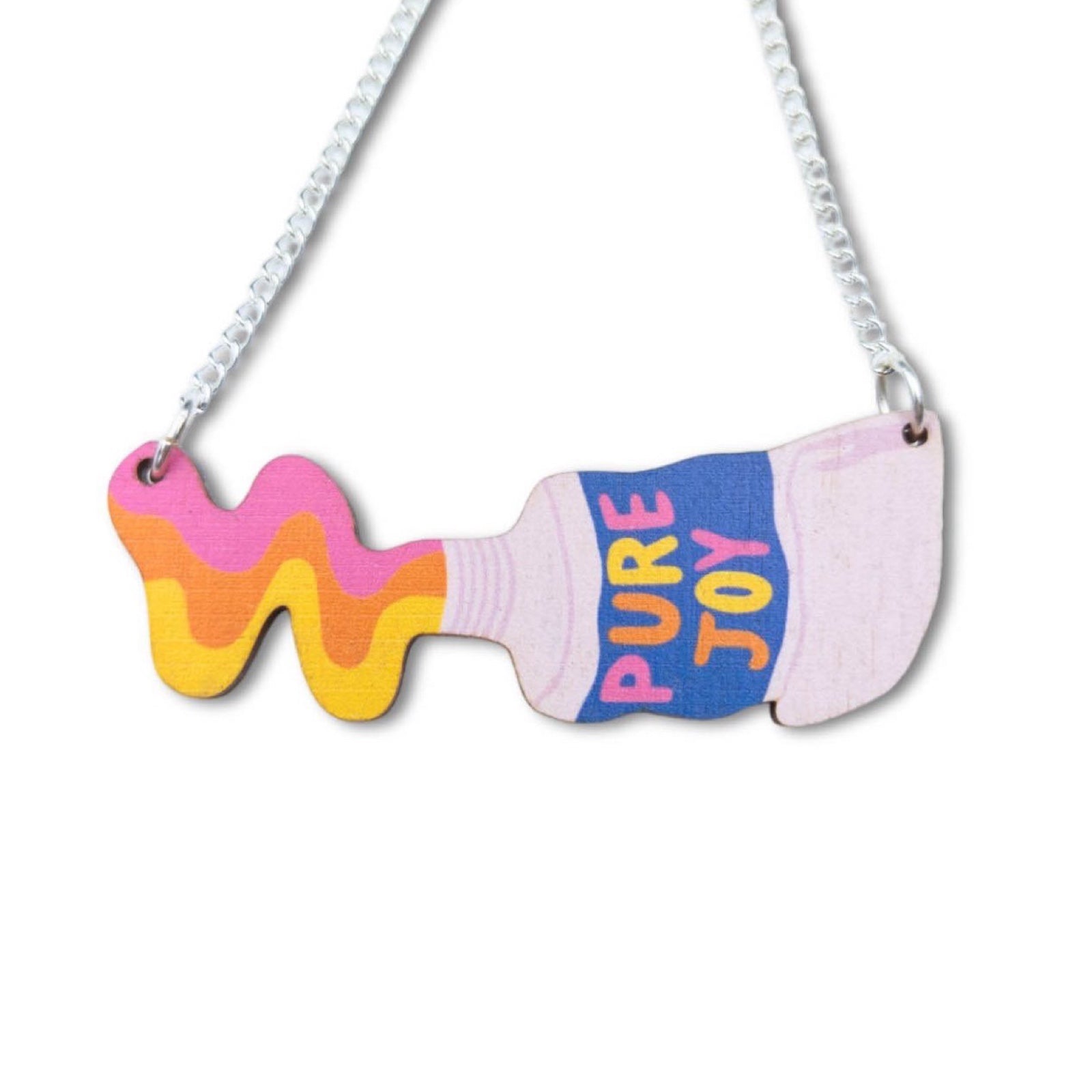 This wooden paint tube necklace features yellow, orange and pink paint being squeezed out of a white tube of paint with the multicoloured text 'Pure Joy' in the centre of the tubes