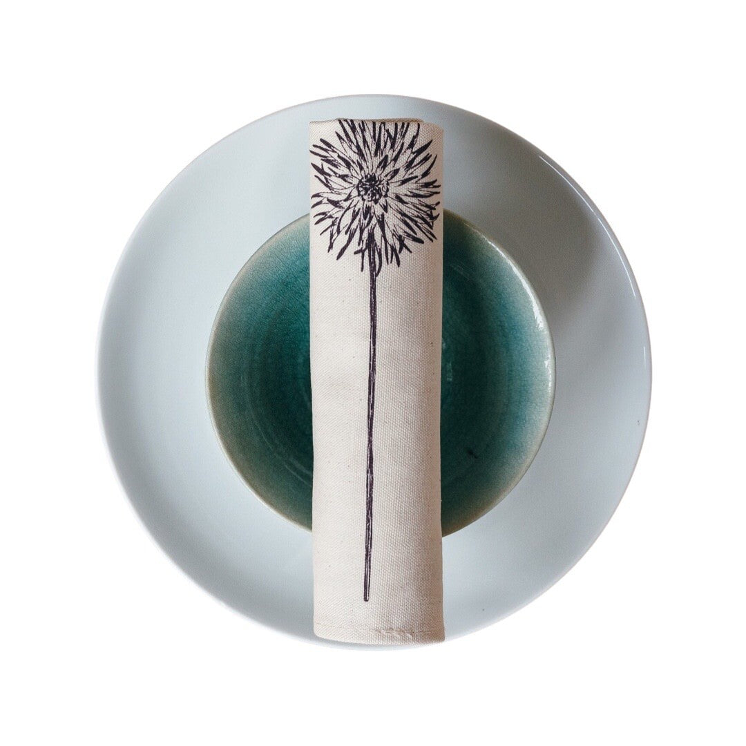 Rolled cream cotton napkin with a screen printed purple dahlia flower.