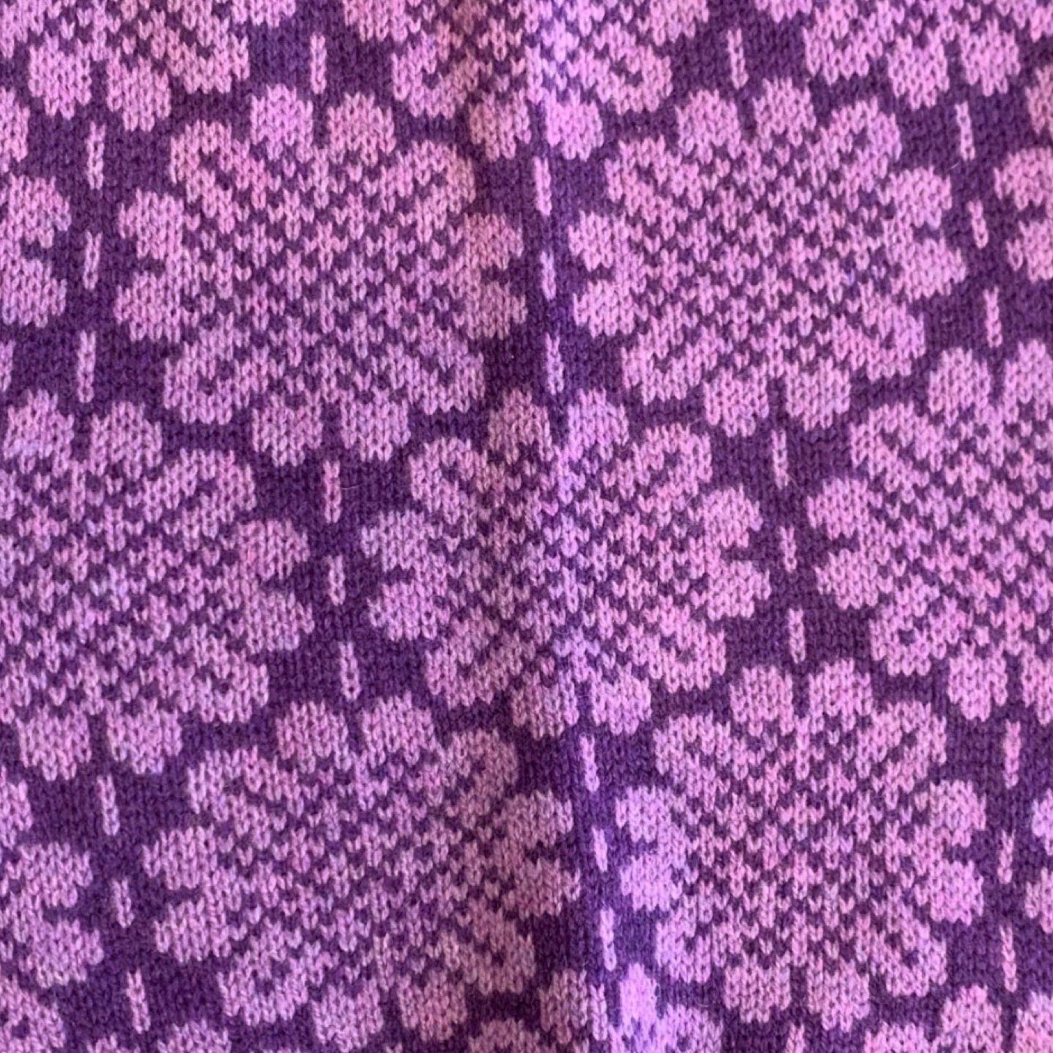 A soft and cosy 100% lambswool knitted snood in a light purple daisy design against a deep purple background.