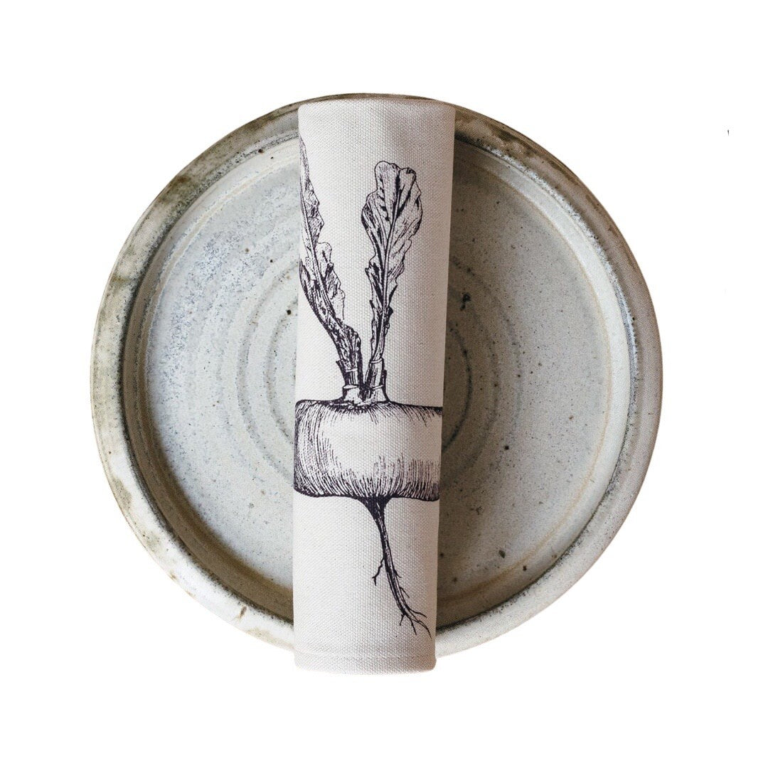 Cream cotton napkin with a purple turnip rolled on a plate.