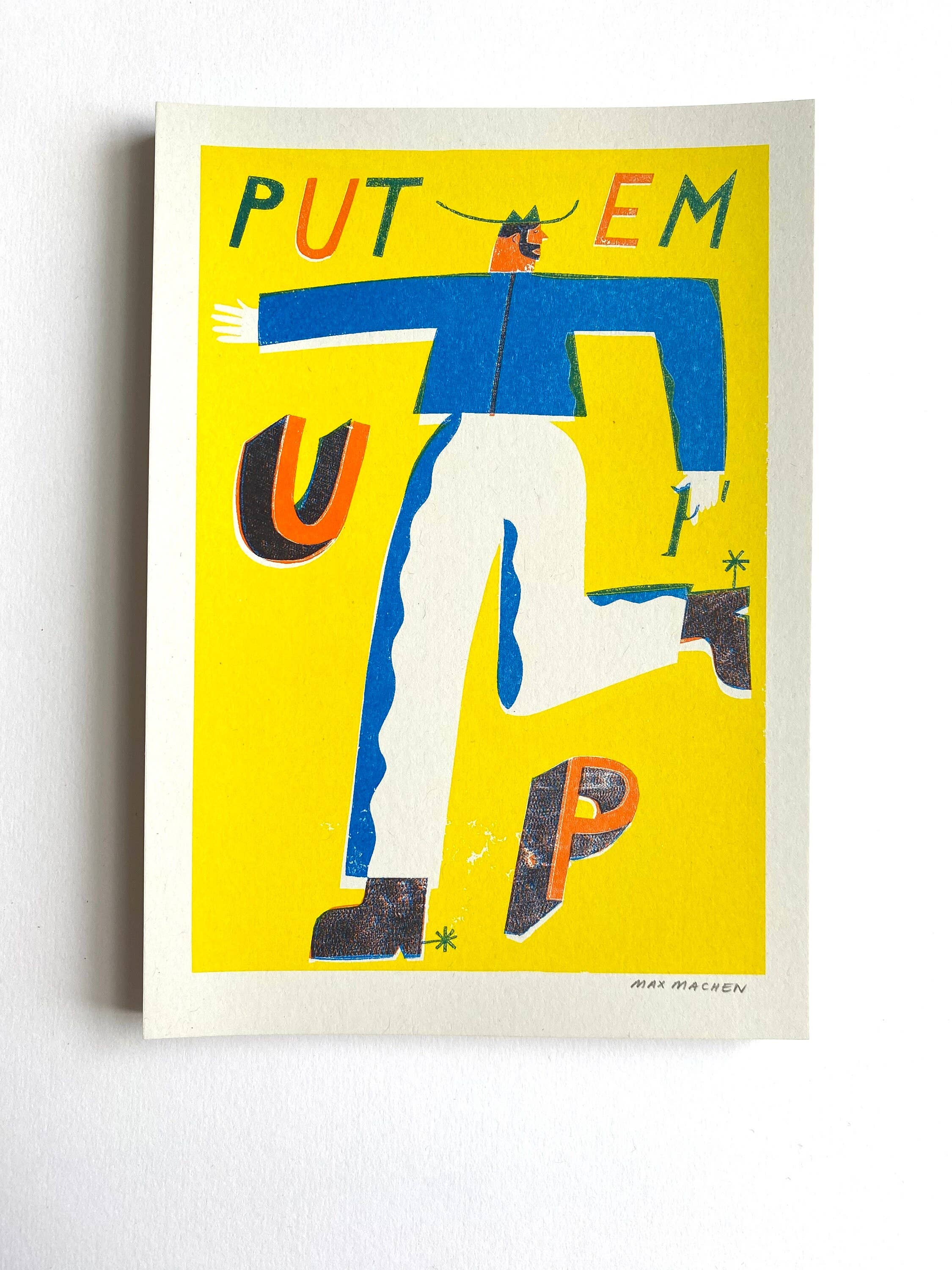 Three-colour risograph print featuring a cowboy wearing a blue shirt and white trousers with the text 'Put Em Up', all against a yellow background.