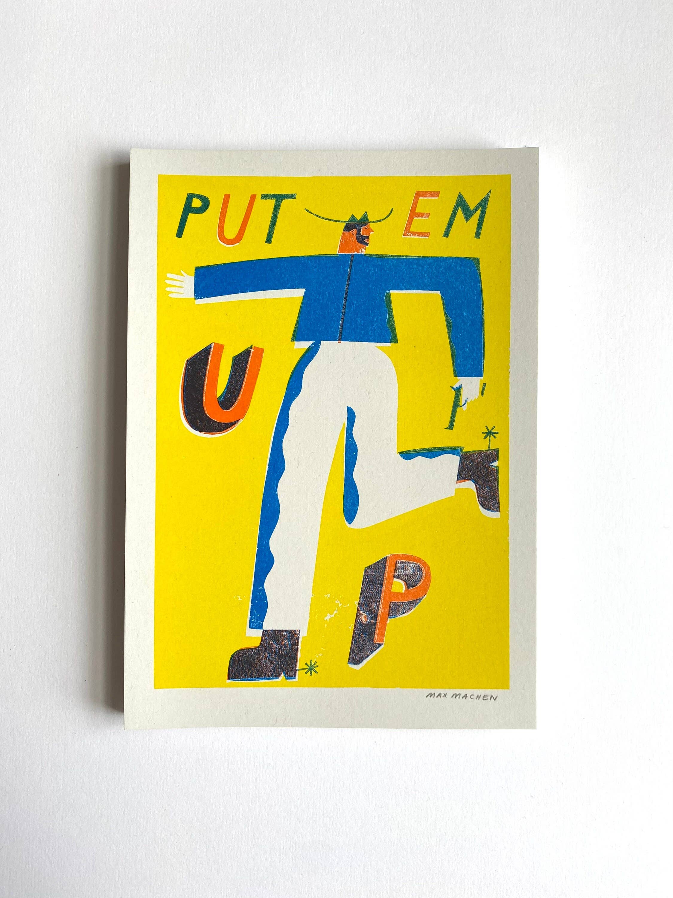 Three-colour risograph print featuring a cowboy wearing a blue shirt and white trousers with the text 'Put Em Up', all against a yellow background.