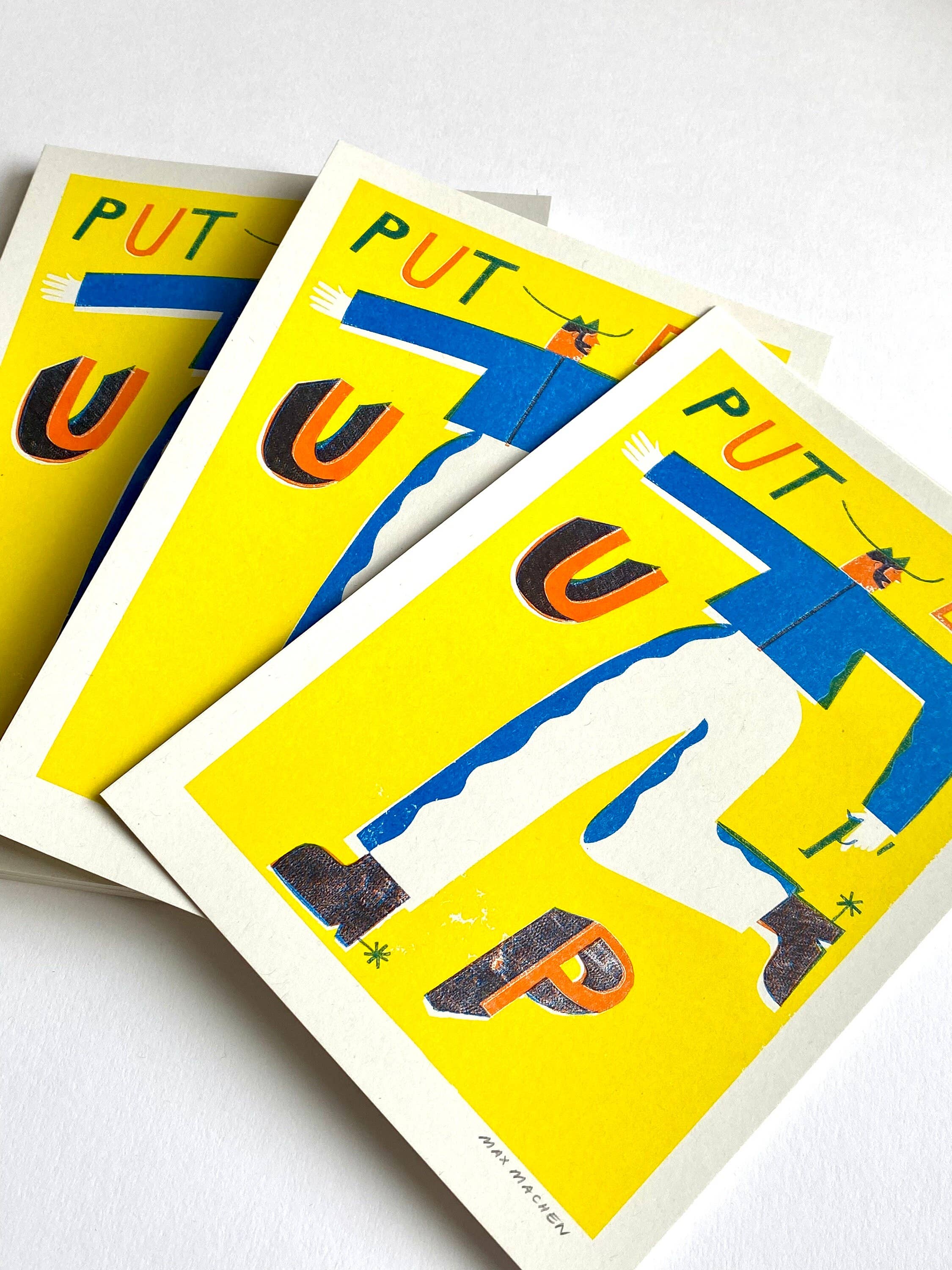 Three-colour risograph print featuring a cowboy wearing a blue shirt and white trousers with the text 'Put Em Up', all against a yellow background.