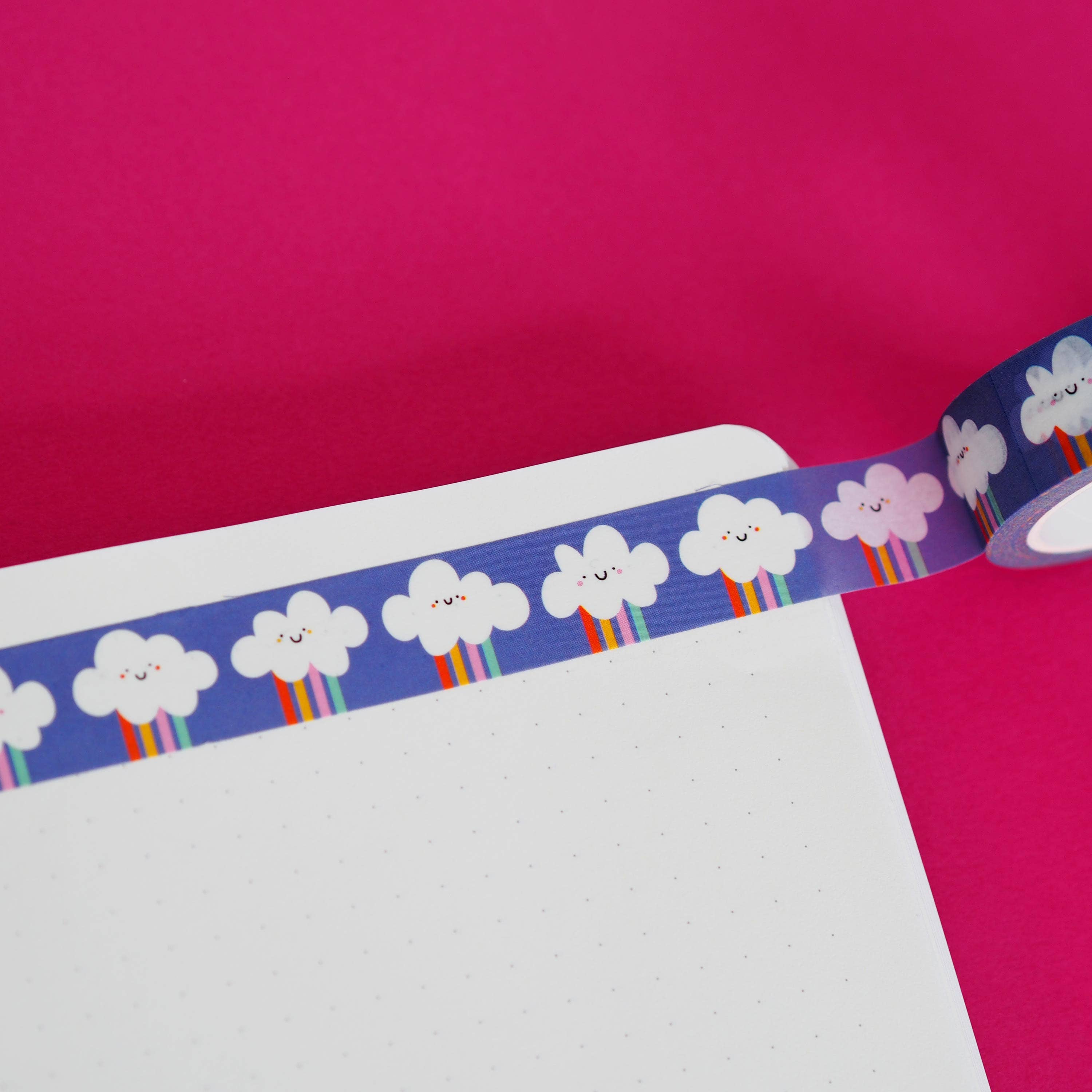 Decorative washi tape with cloud and rainbow design on a pink background.