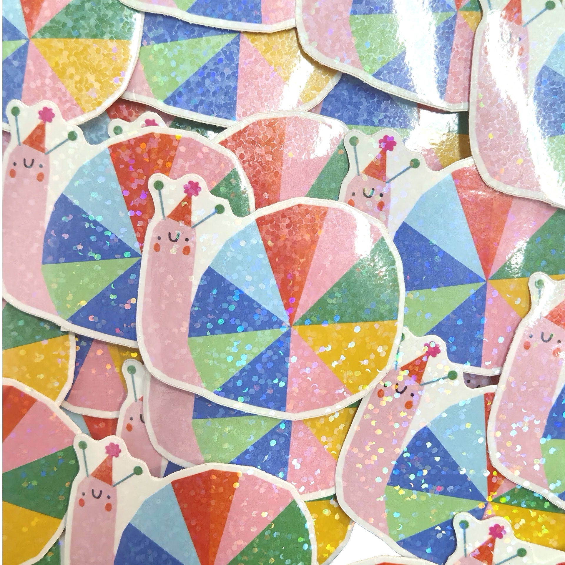 A pile of colourful stickers featuring cute pink snail characters wearing party hats, set against a background of overlapping triangular patterned stickers.