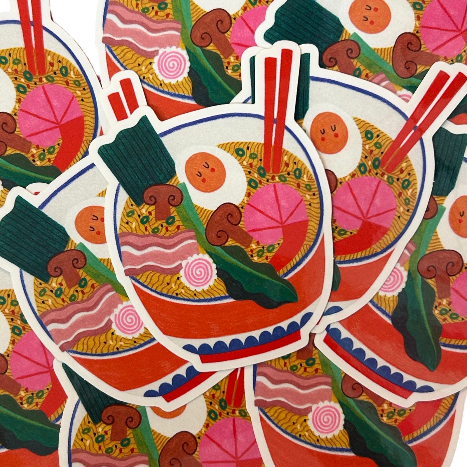 A pile of stickers featuring a colourful, whimsical illustration of a bowl of ramen with chopsticks, a half-egg, vegetables and prawns.
