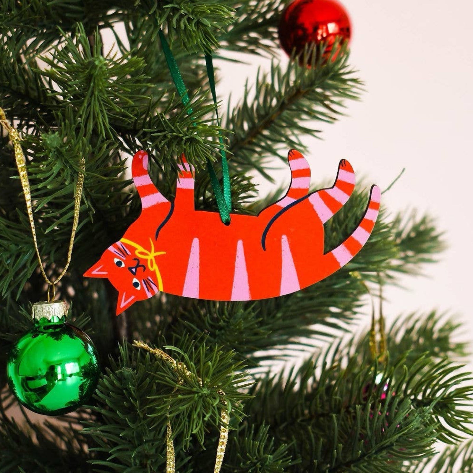 Wooden Christmas cat-shaped decoration in red with pink stripes on tree.