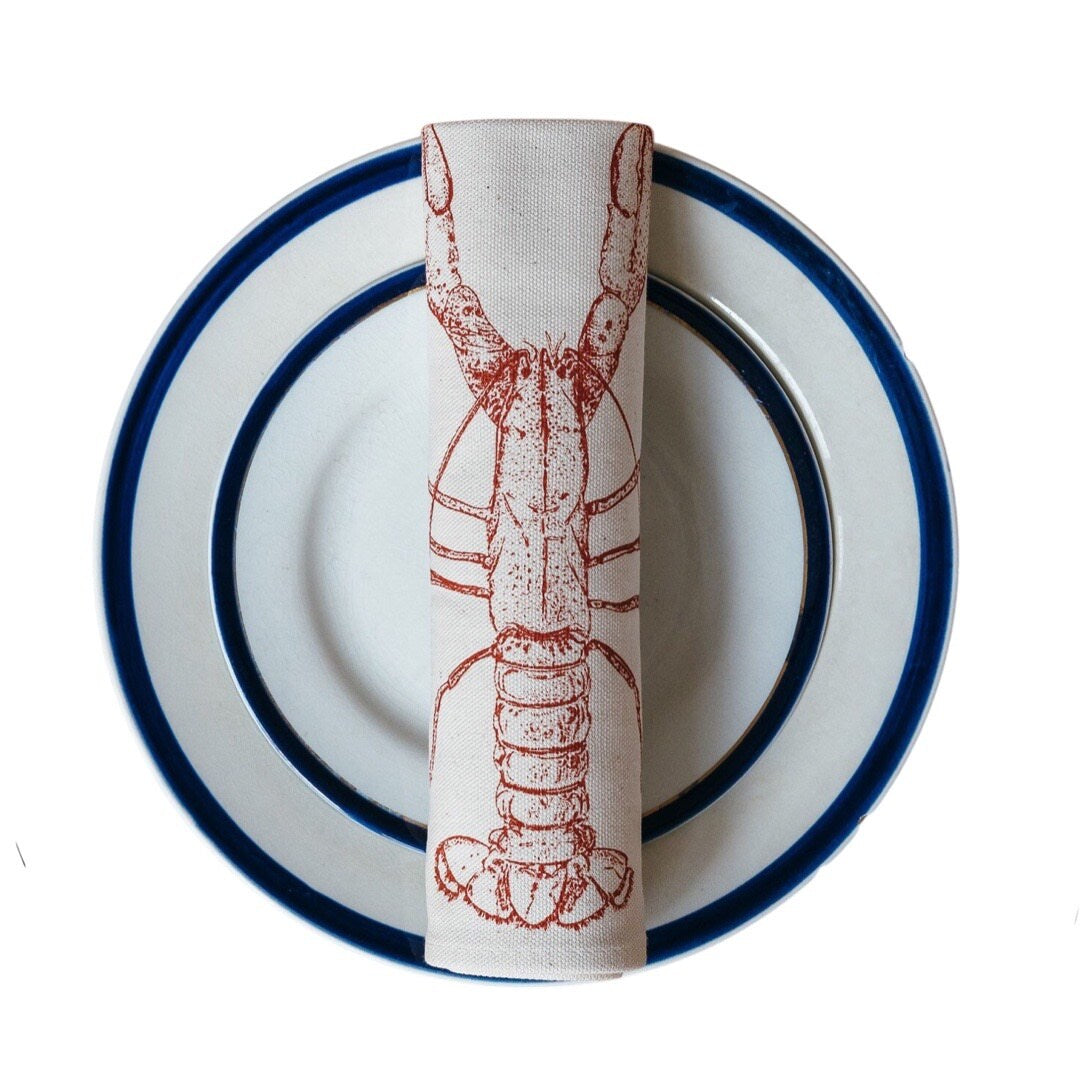 Cream cotton napkin with a red lobster rolled and sitting on a plate.