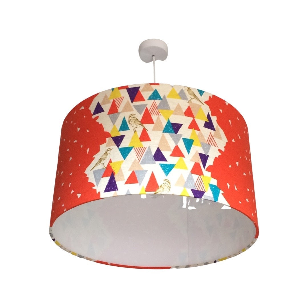 Drum lampshade covered in Echino cotton featuring a red background with panels of multicolured triangles and light brown birds.