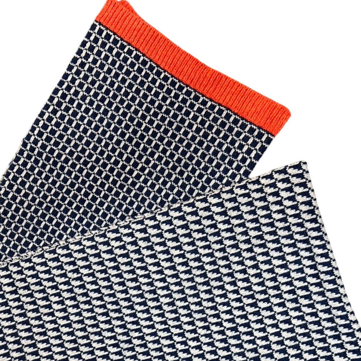 A close-up of a folded knit scarf with a navy and white pattern and a bright orange ribbed cuff, shown on a plain white background.