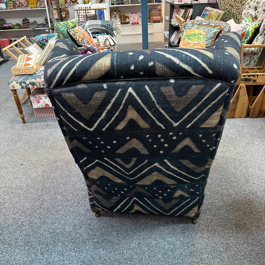 A high-back armchair upholstered in a dark navy blue fabric with a beige and cream geometric tribal pattern, photographed in a furniture store.