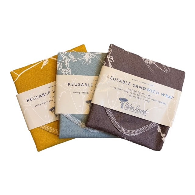 Three reusable sandwich wraps in duck egg blue, grey, and mustard colors, laid flat with visible branding and design.