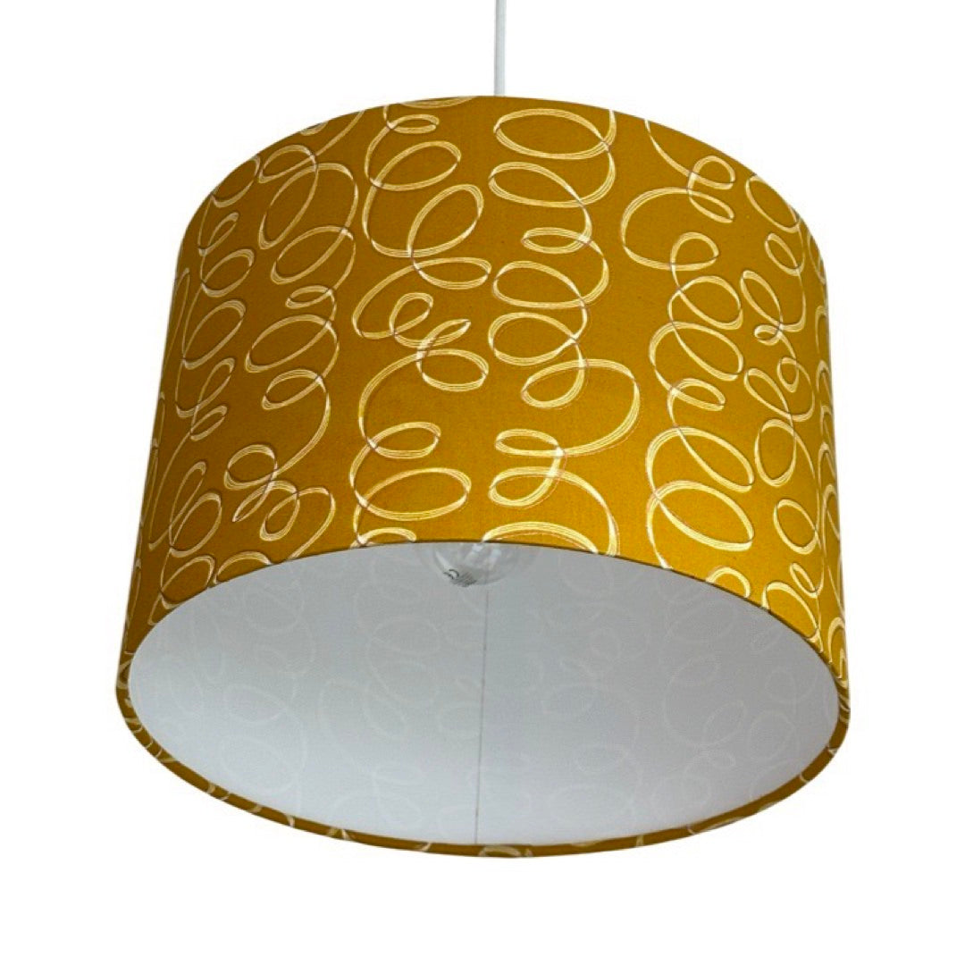 Close up of a drum lampshade covered in mustard cotton fabric with white and gold ribbons.