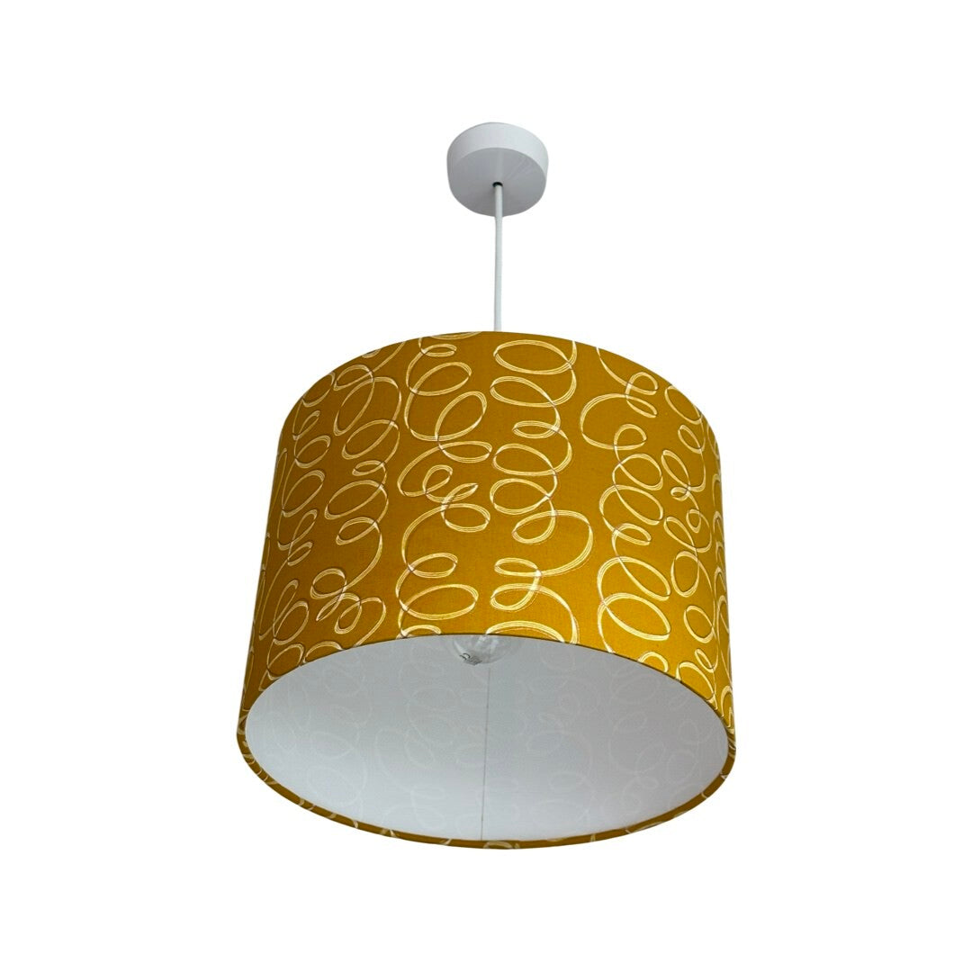 Drum lampshade covered in mustard cotton fabric with white and gold ribbons.