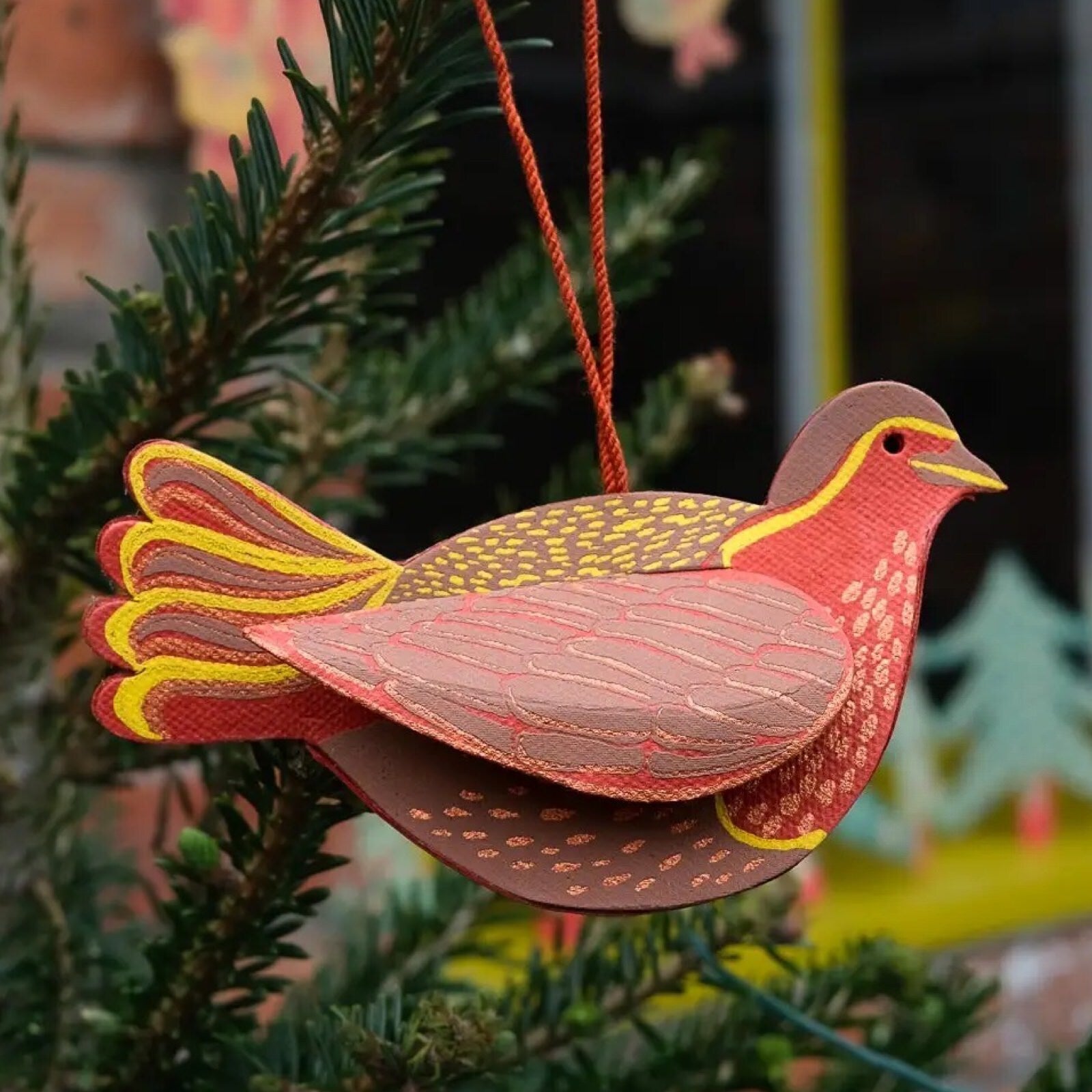 A red robin three-dimensional cardboard decoration hanging on a Christmas tree.