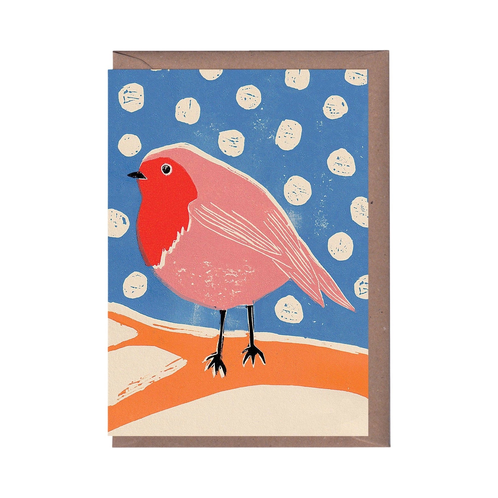 A greeting card featuring a stylised pink robin bird on an orange ground against a blue sky with white polka dots, shown with a brown envelope behind it on a white background.