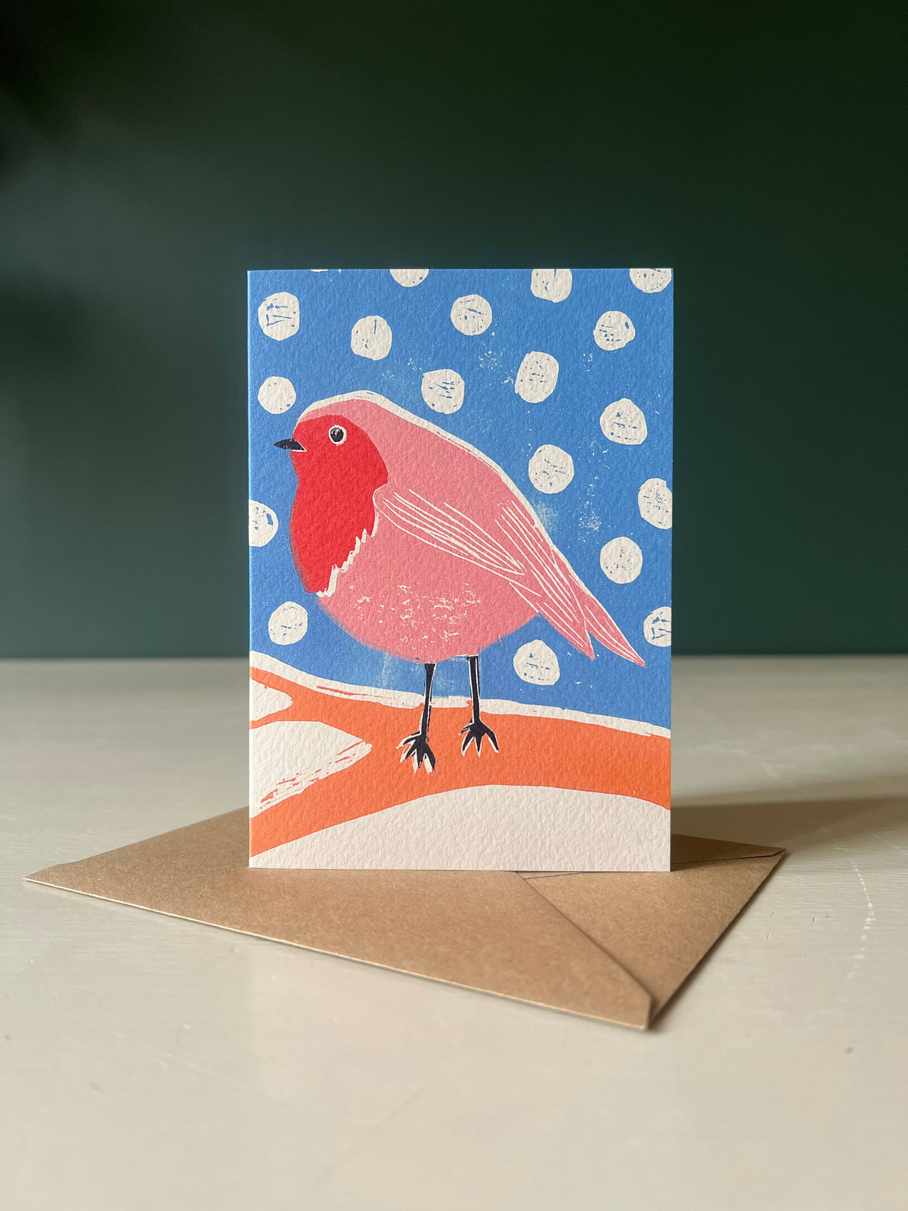 Greeting card with a red robin design on a blue background with white dots, accompanied by a brown envelope.