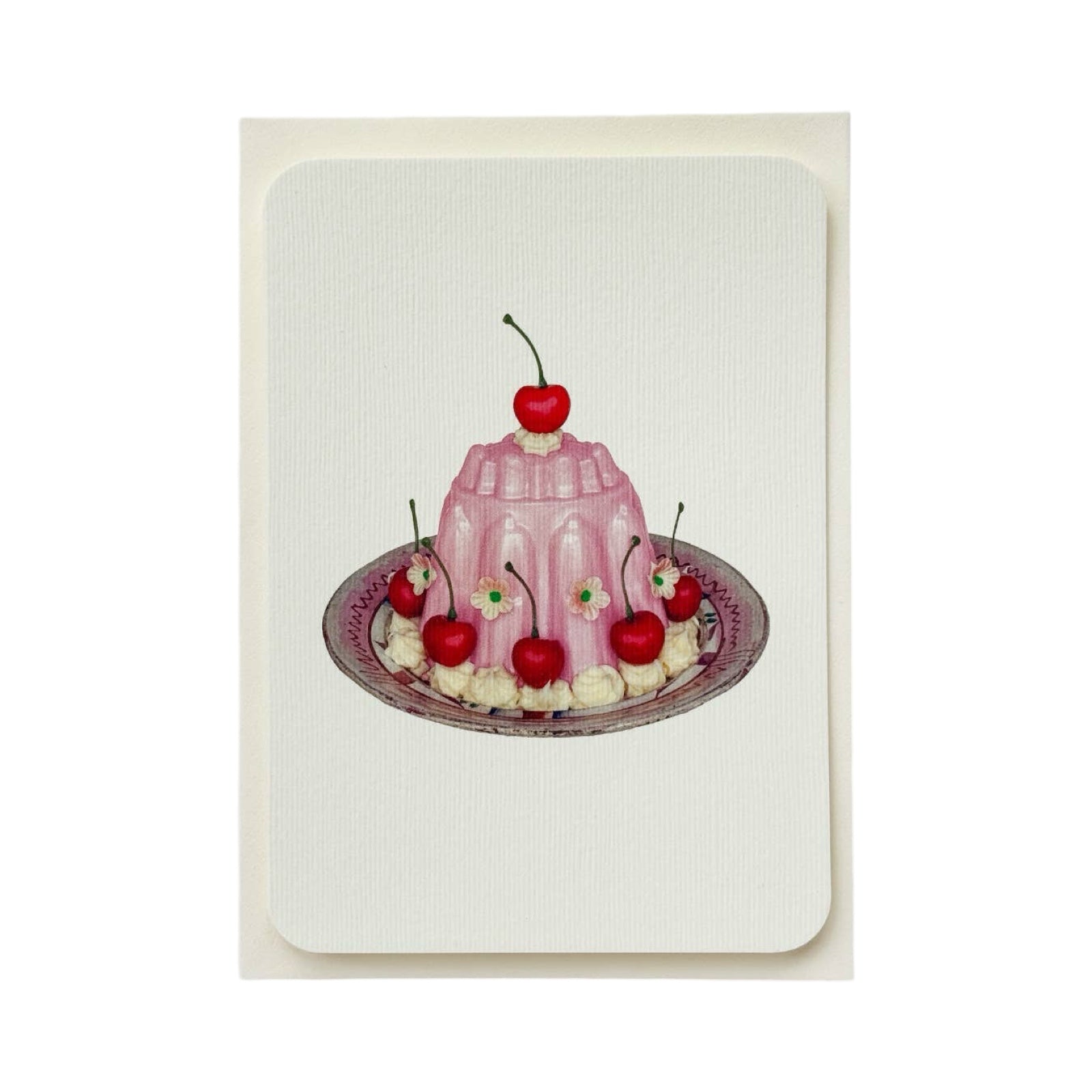 A cream coloured birthday card with a pink blancmange with cherries, cream and small pink flowers, all on a white and pink plate.