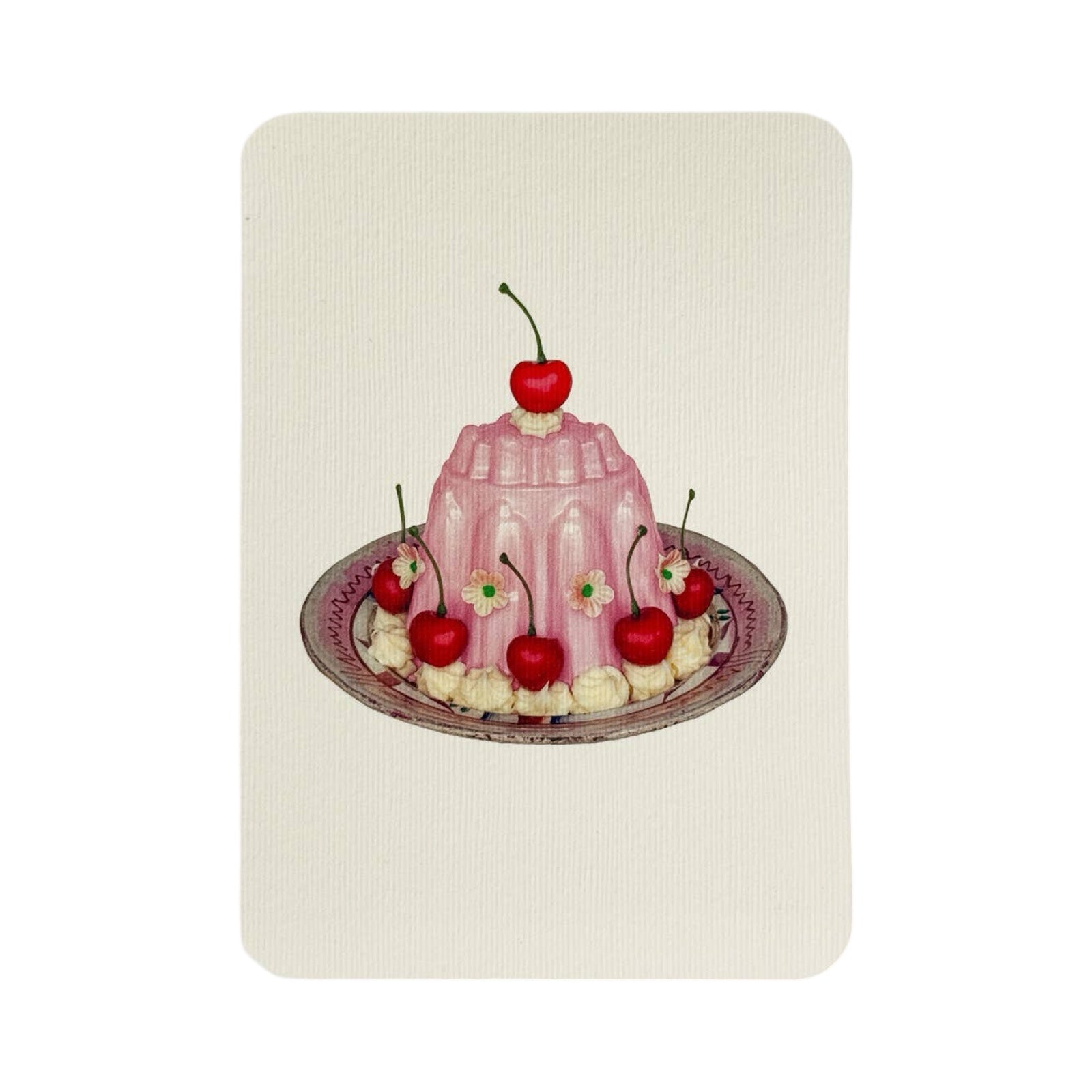A cream coloured birthday card with a pink blancmange with cherries, cream and small pink flowers, all on a white and pink plate.
