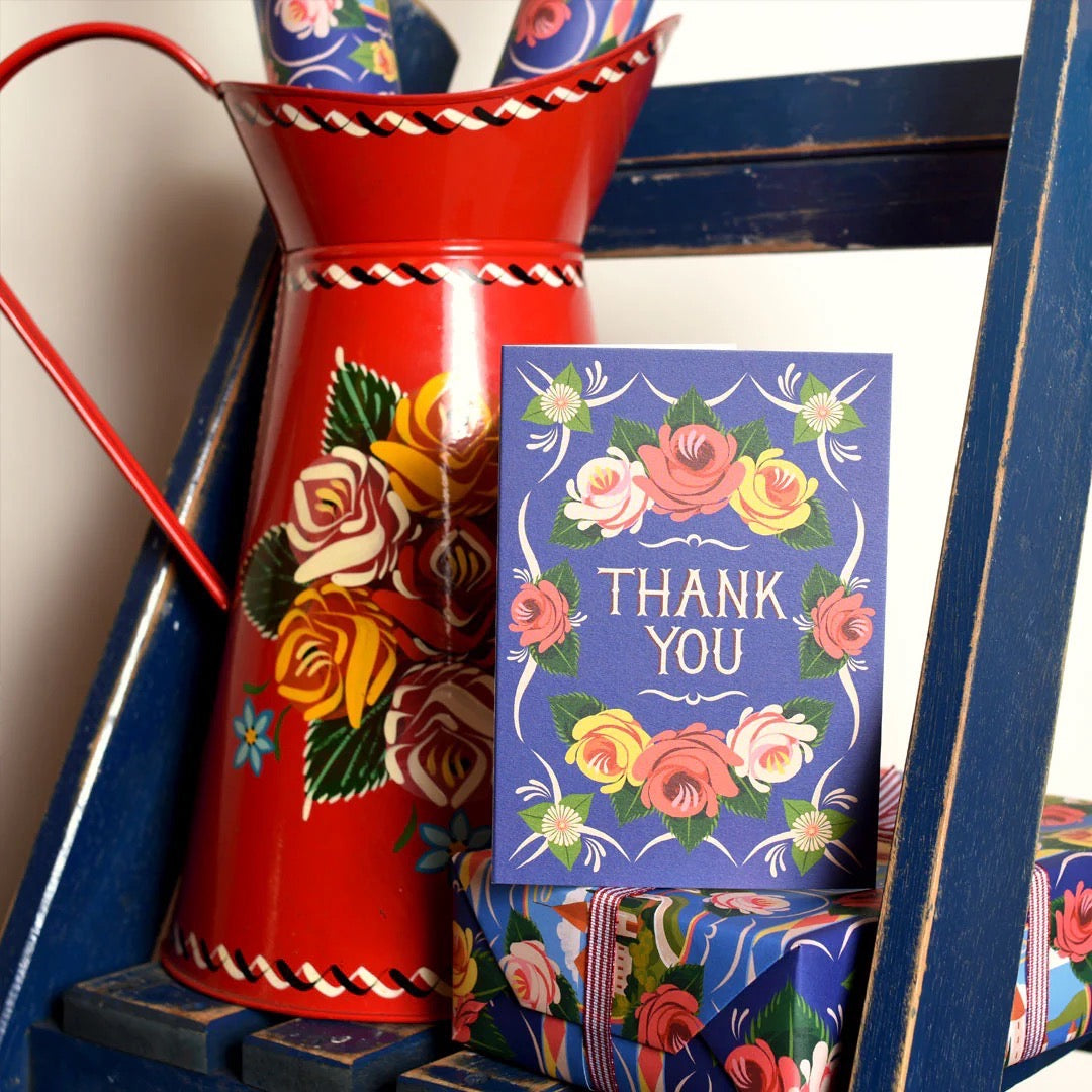 Decorative red vase with floral patterns next to a 'Thank You' card on a blue ladder.