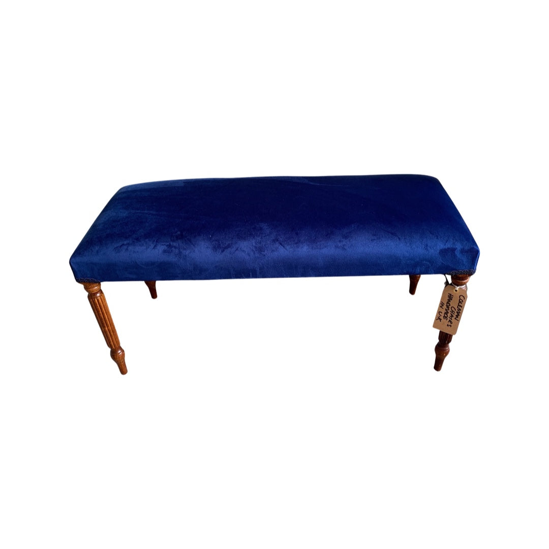 A rectangular velvet bench with mahogany stained legs in a royal blue colour design.