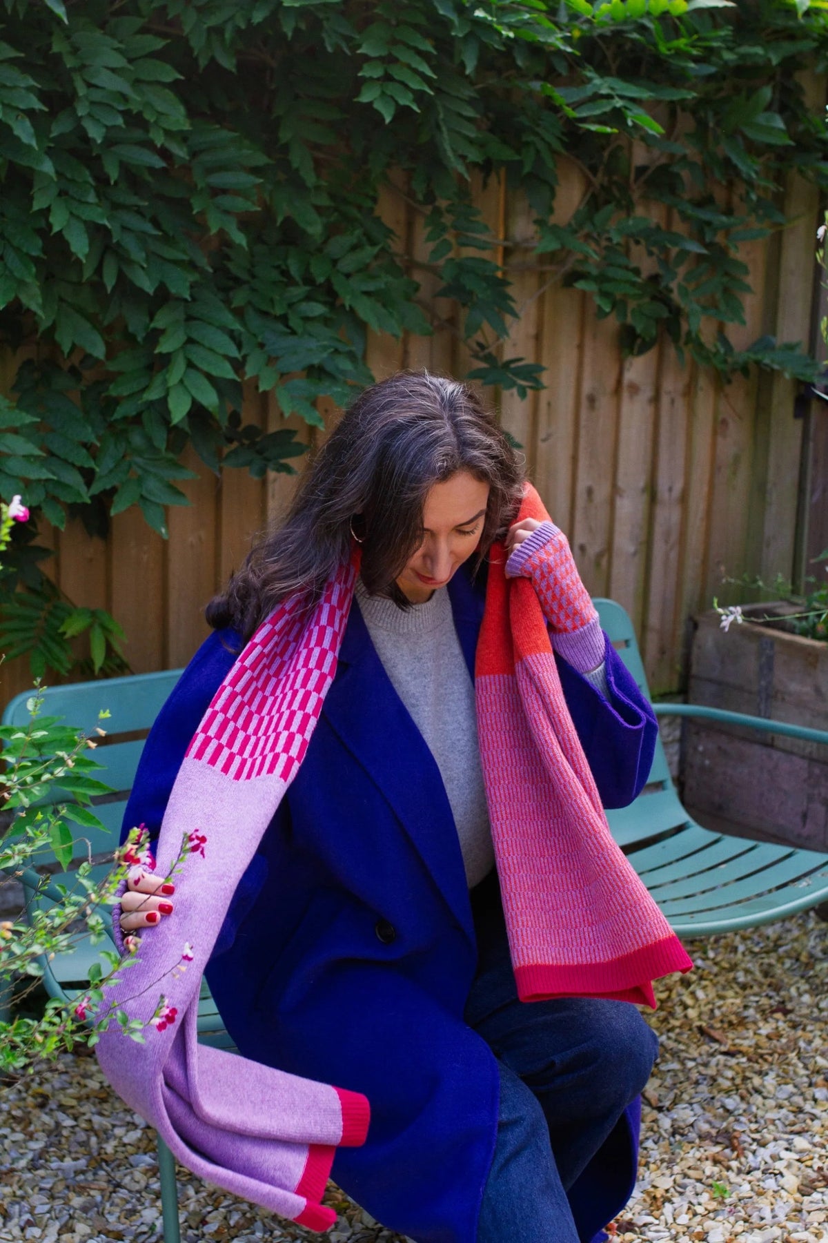 Woman sitting on a bench holding a colorful scarf with a garden background.